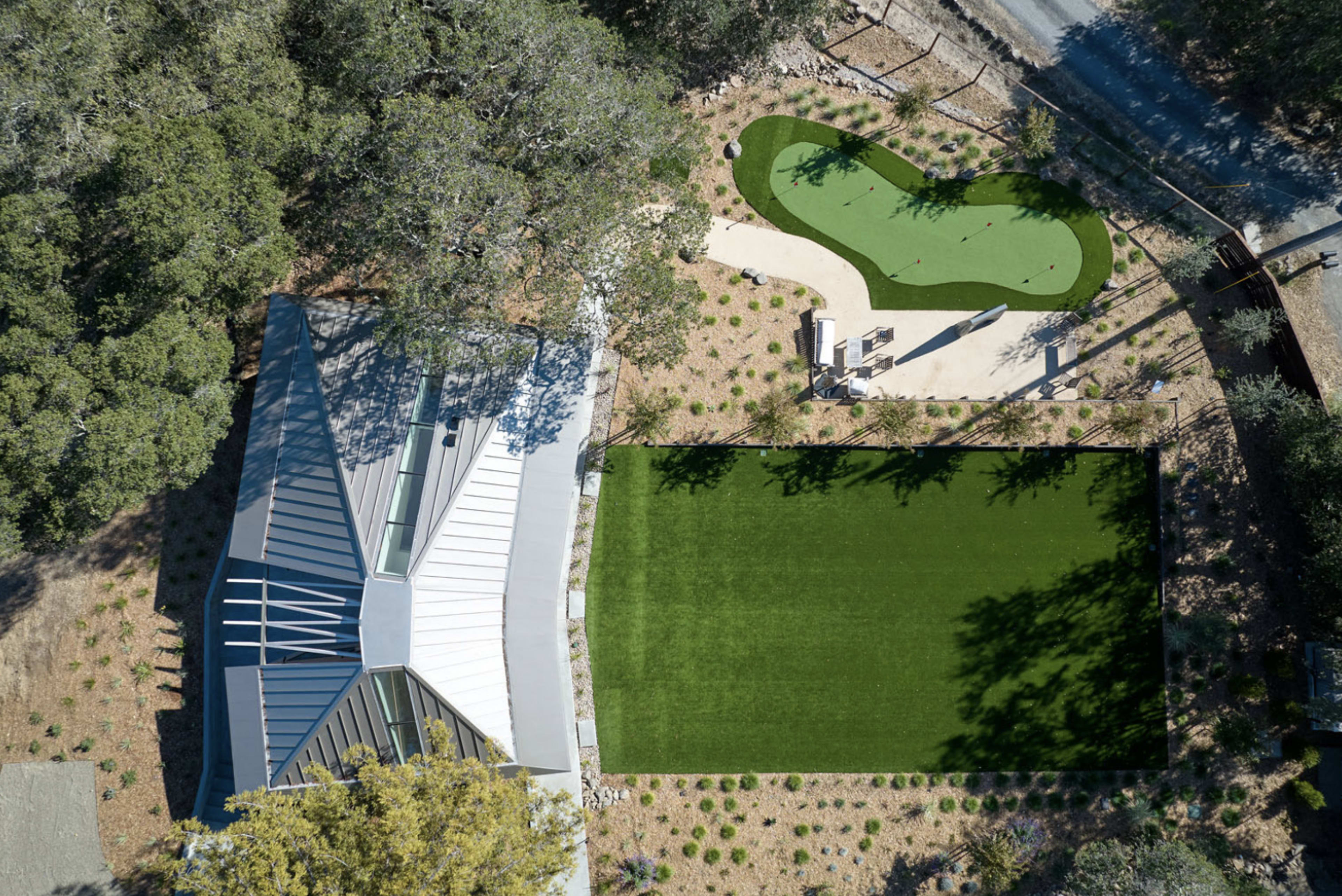 An aerial view of a modern house surrounded by landscaped areas, featuring a green lawn and a small putting green.