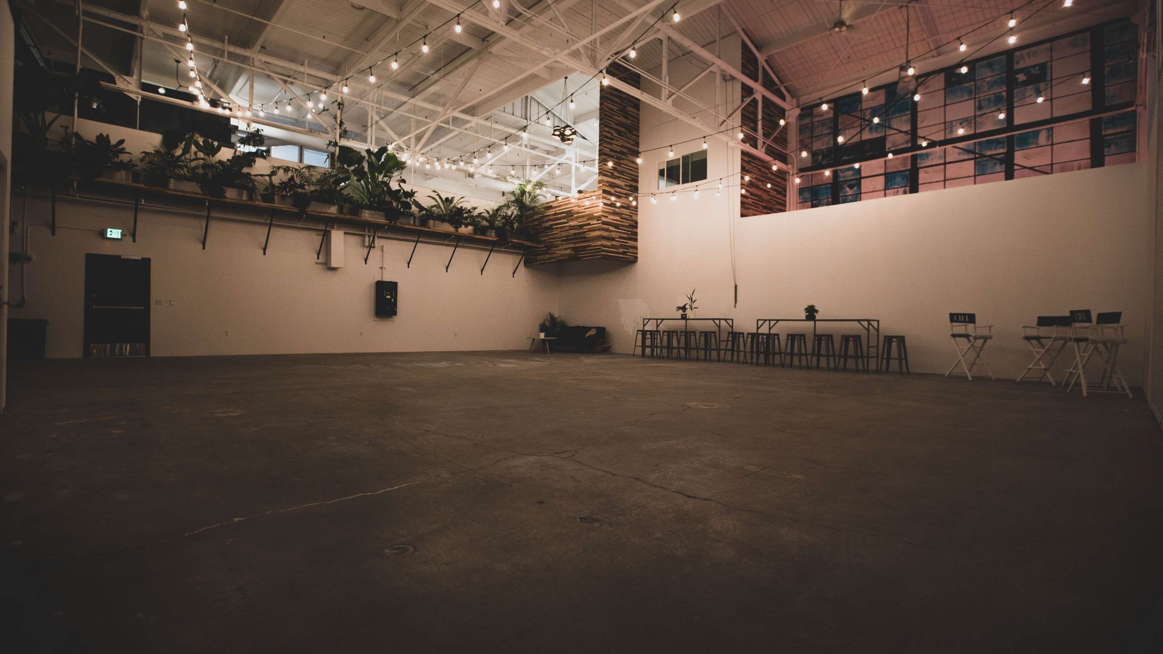 A spacious indoor venue with polished concrete flooring, hanging plants, and multiple seating arrangements.
