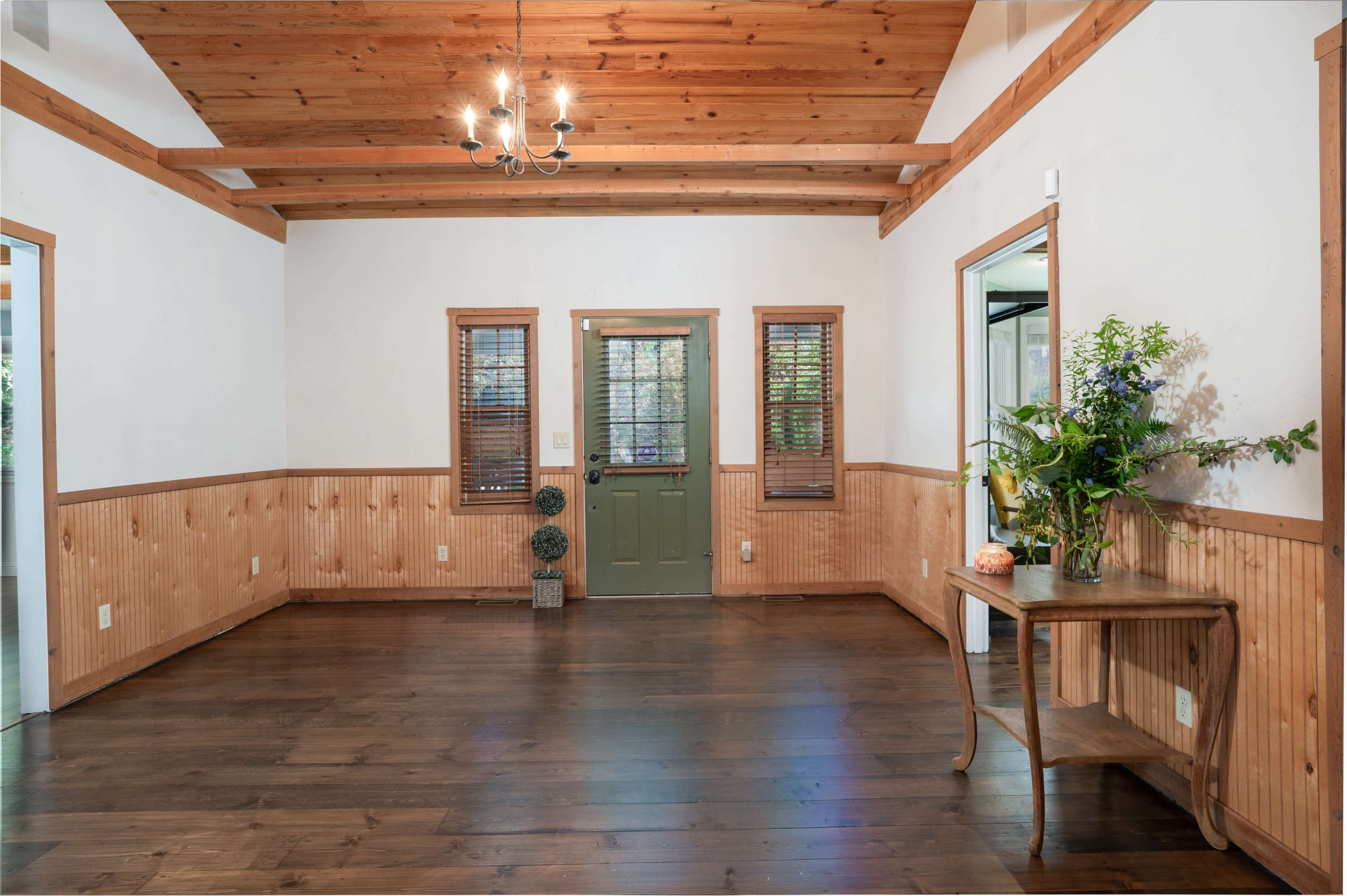 The image shows a spacious room with wooden beams on the ceiling, a wooden floor, and walls partially covered with light-colored paneling.