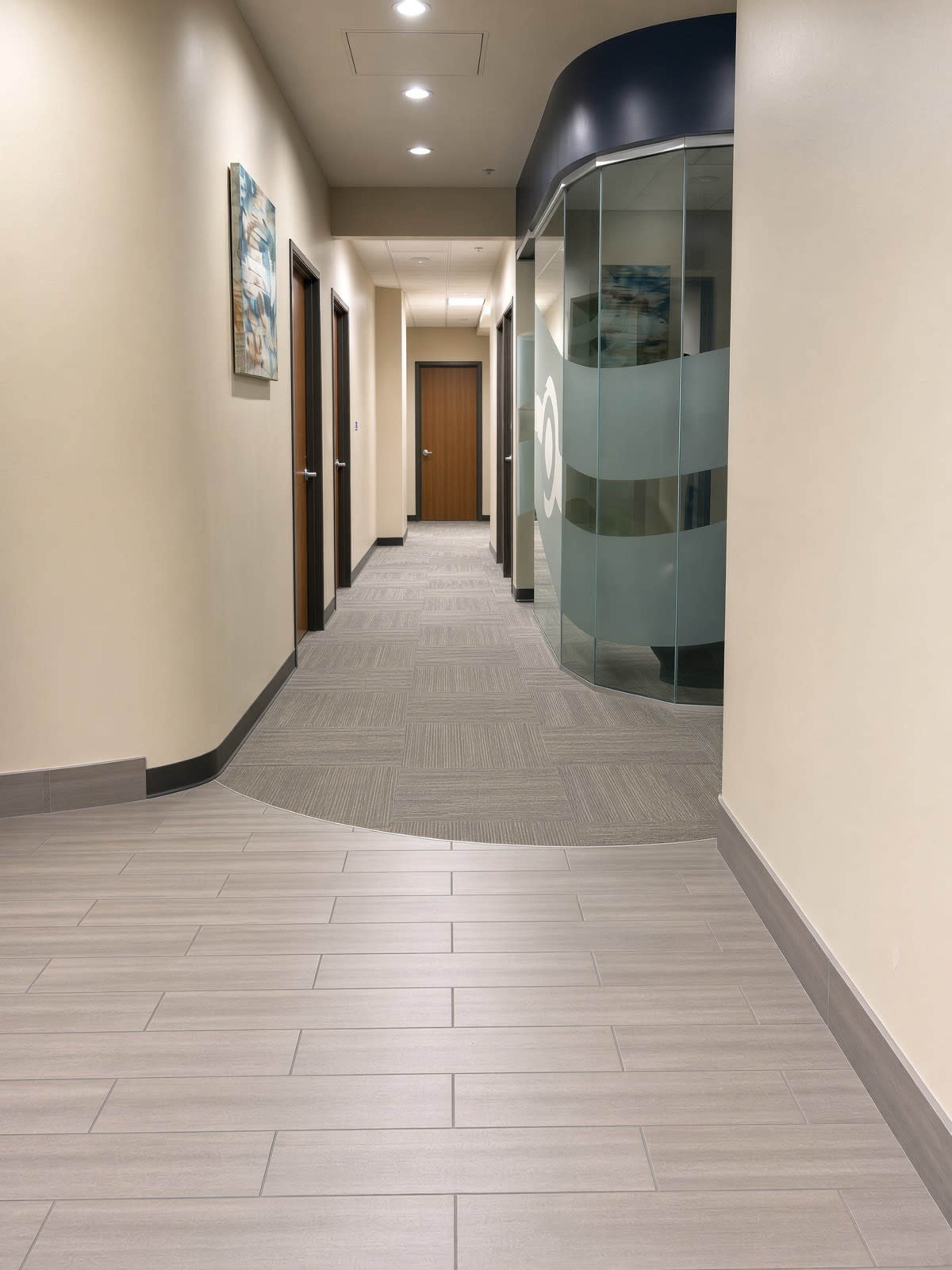 The image shows a well-lit corridor with doors on either side and a curved glass partition at the end.