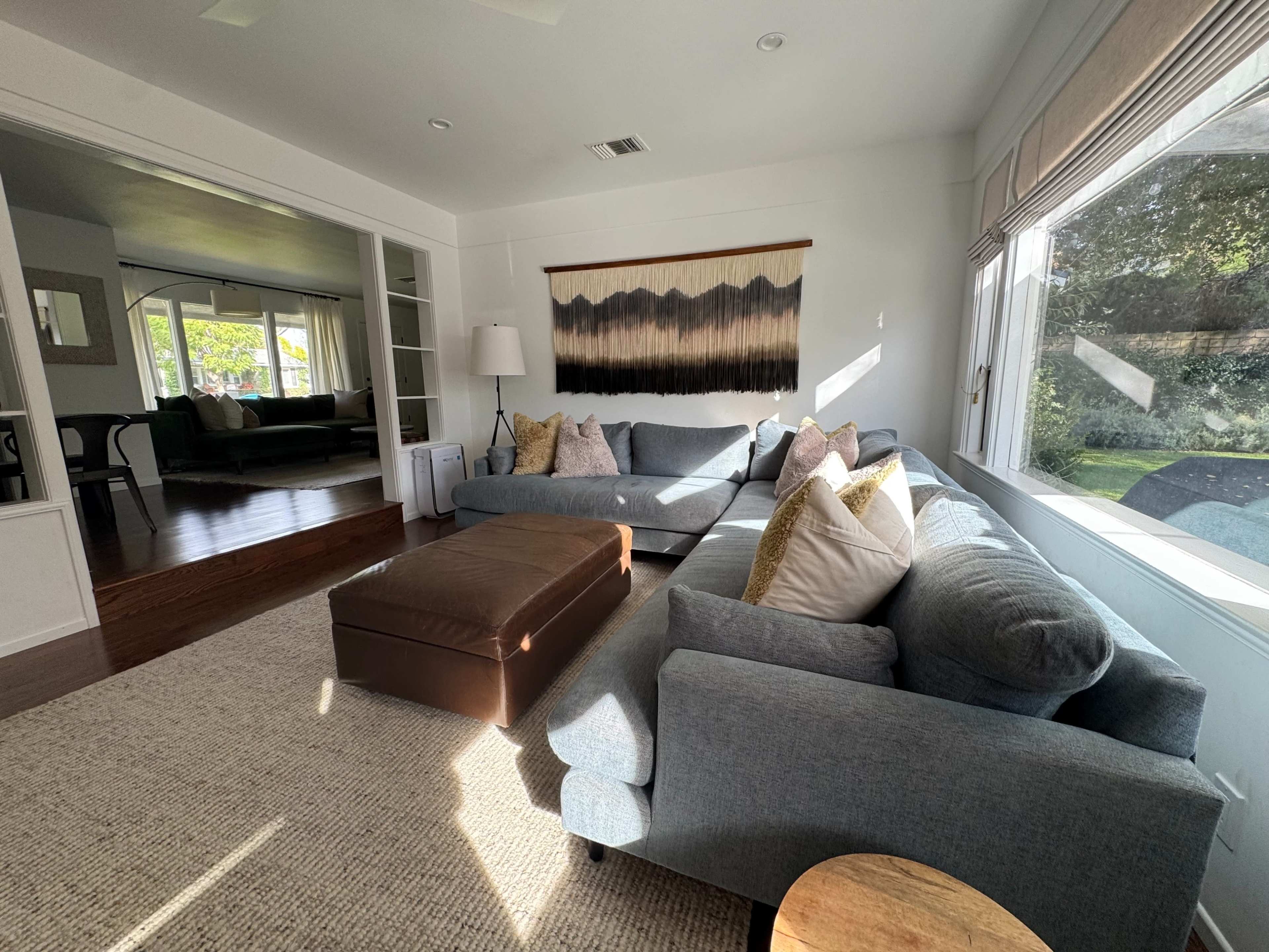 The image shows a bright living room featuring two sofas, a coffee table, and a large window with natural light streaming in.