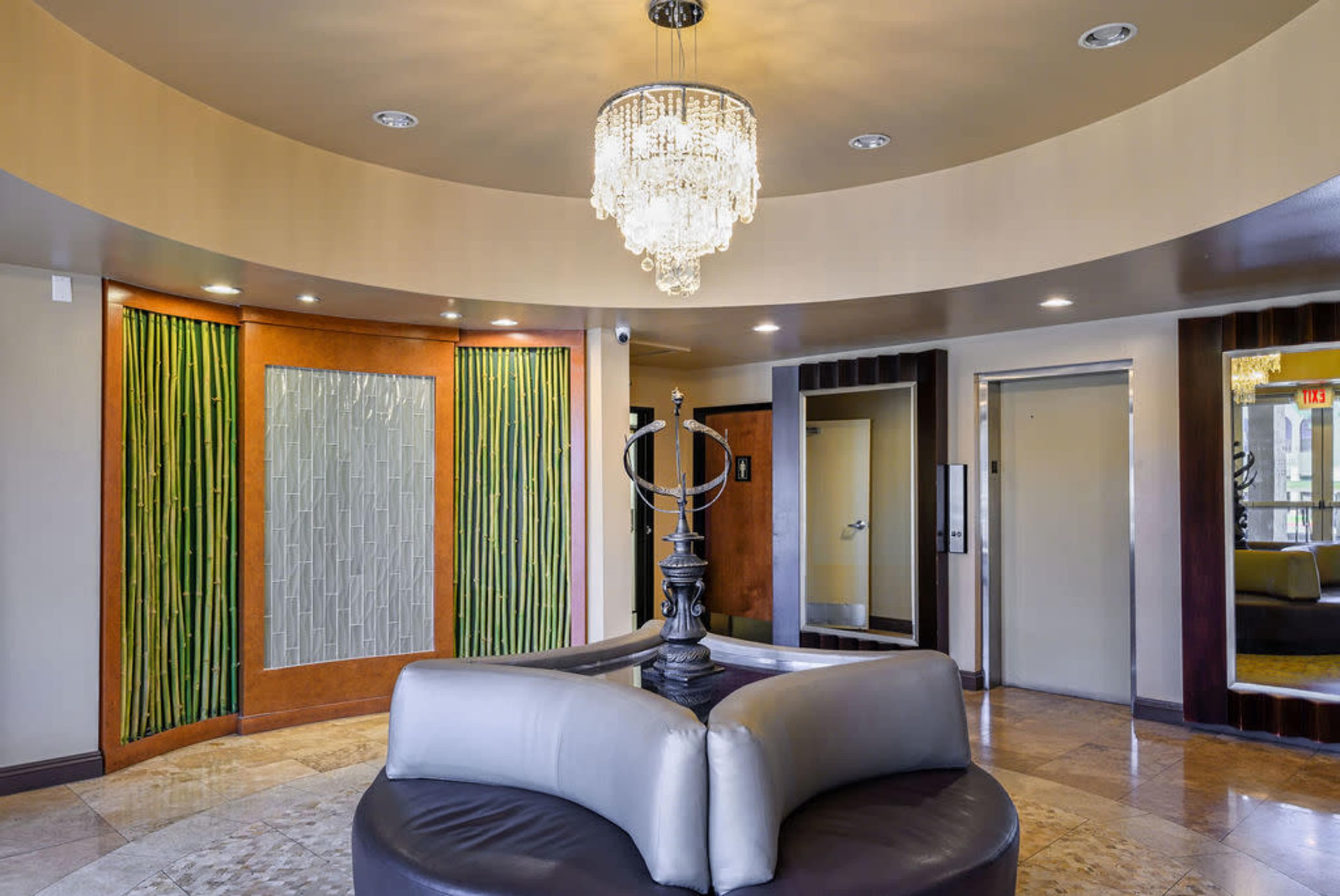 The image shows a circular lobby area featuring a chandelier, a central seating arrangement, and decorative wall panels with a mix of materials.