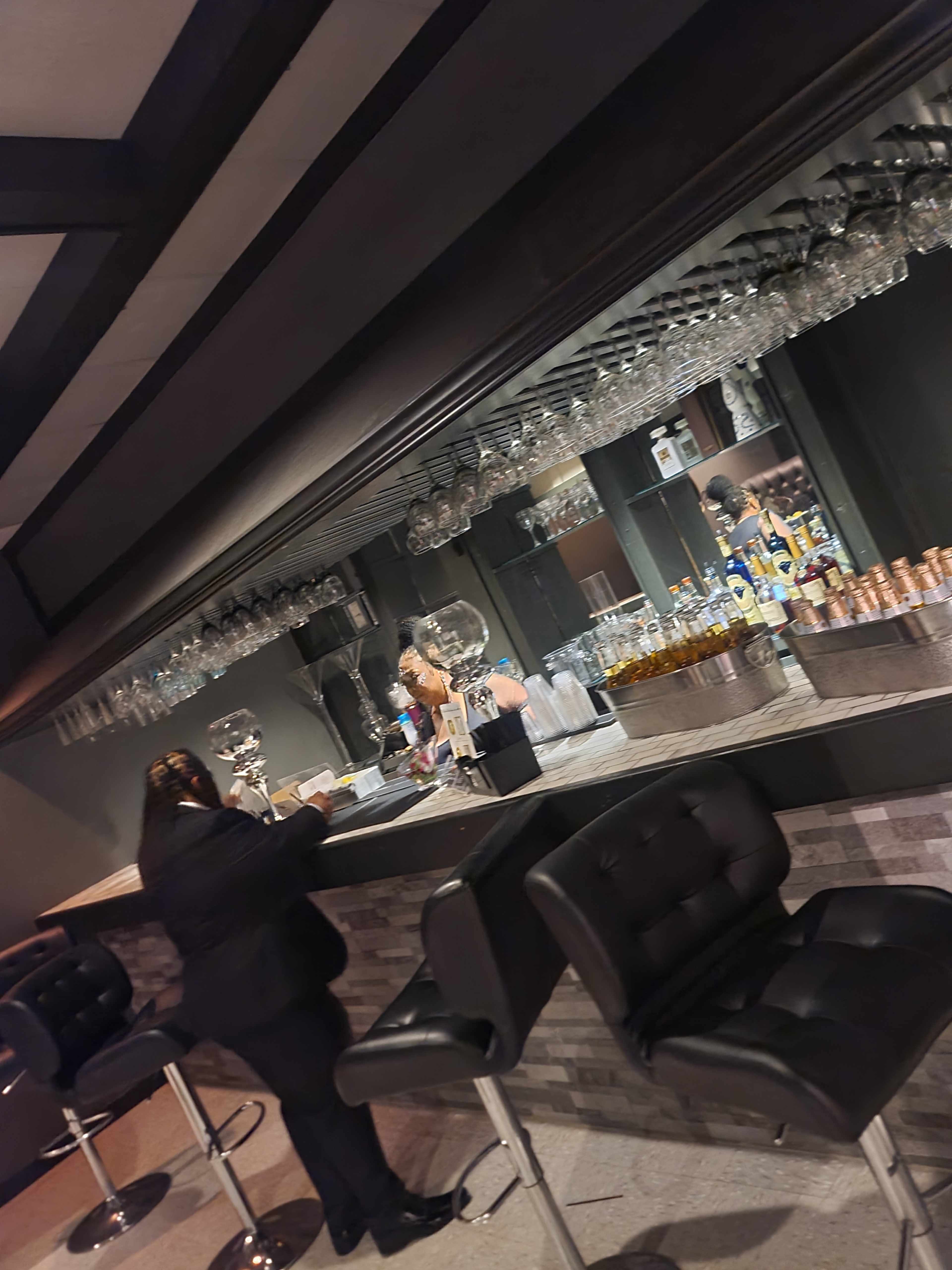 A bartender serves drinks at a modern bar with glassware hanging above and a sleek counter.