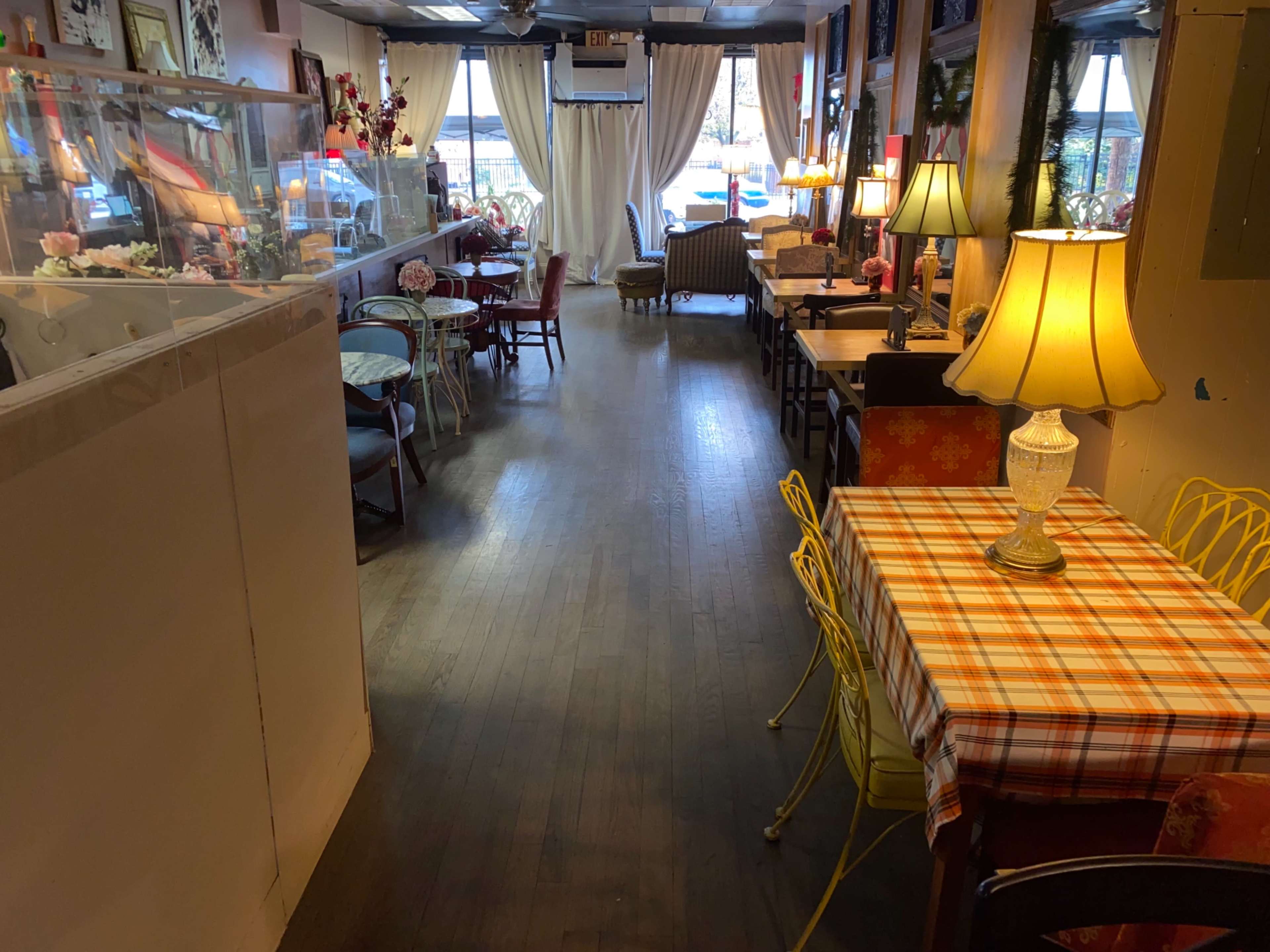 A cozy café interior with wooden flooring, tables of varying styles, and soft lighting from lamps placed around the space.