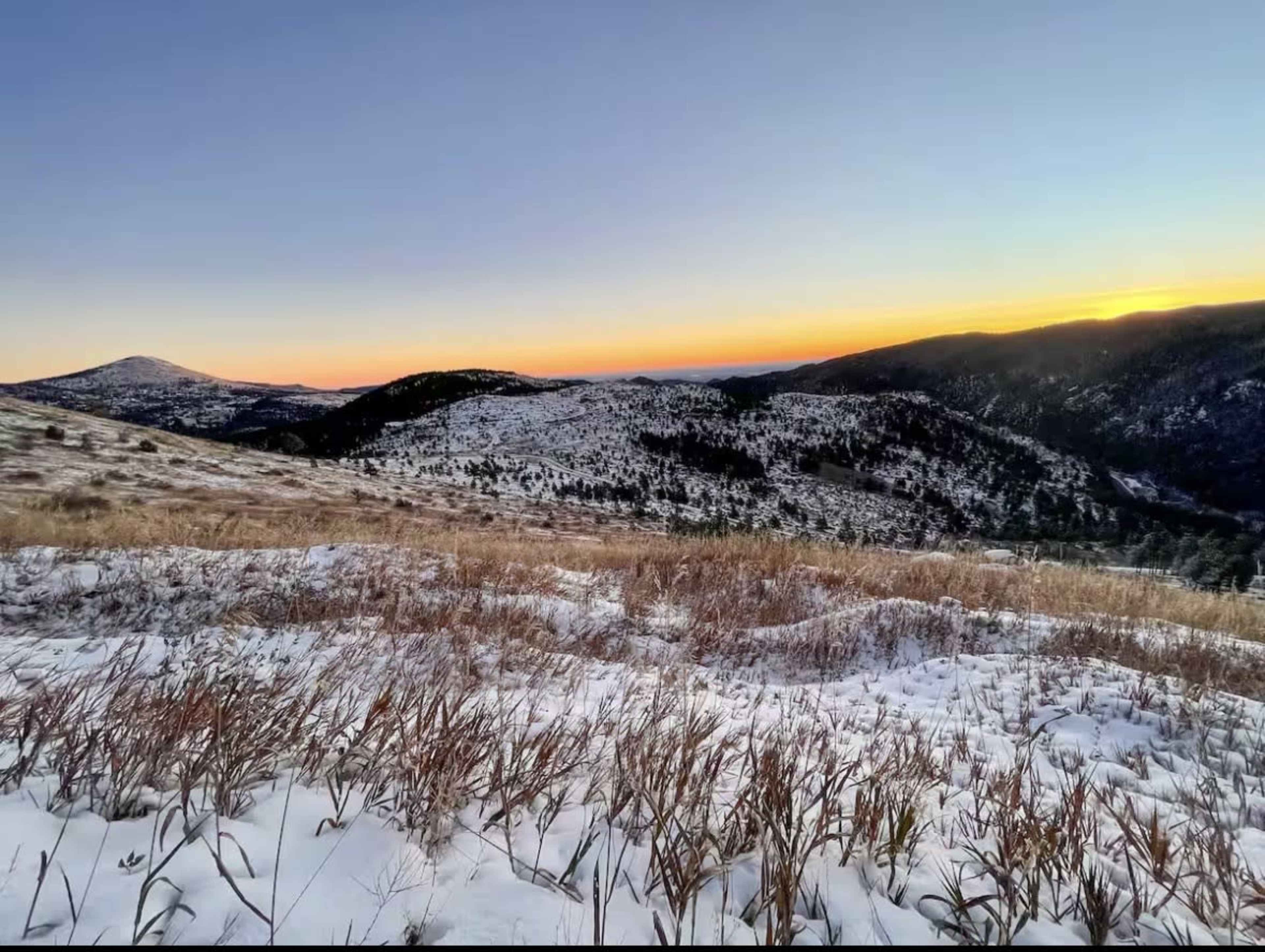 The image shows a snowy landscape with rolling hills and a sunset sky in the background.