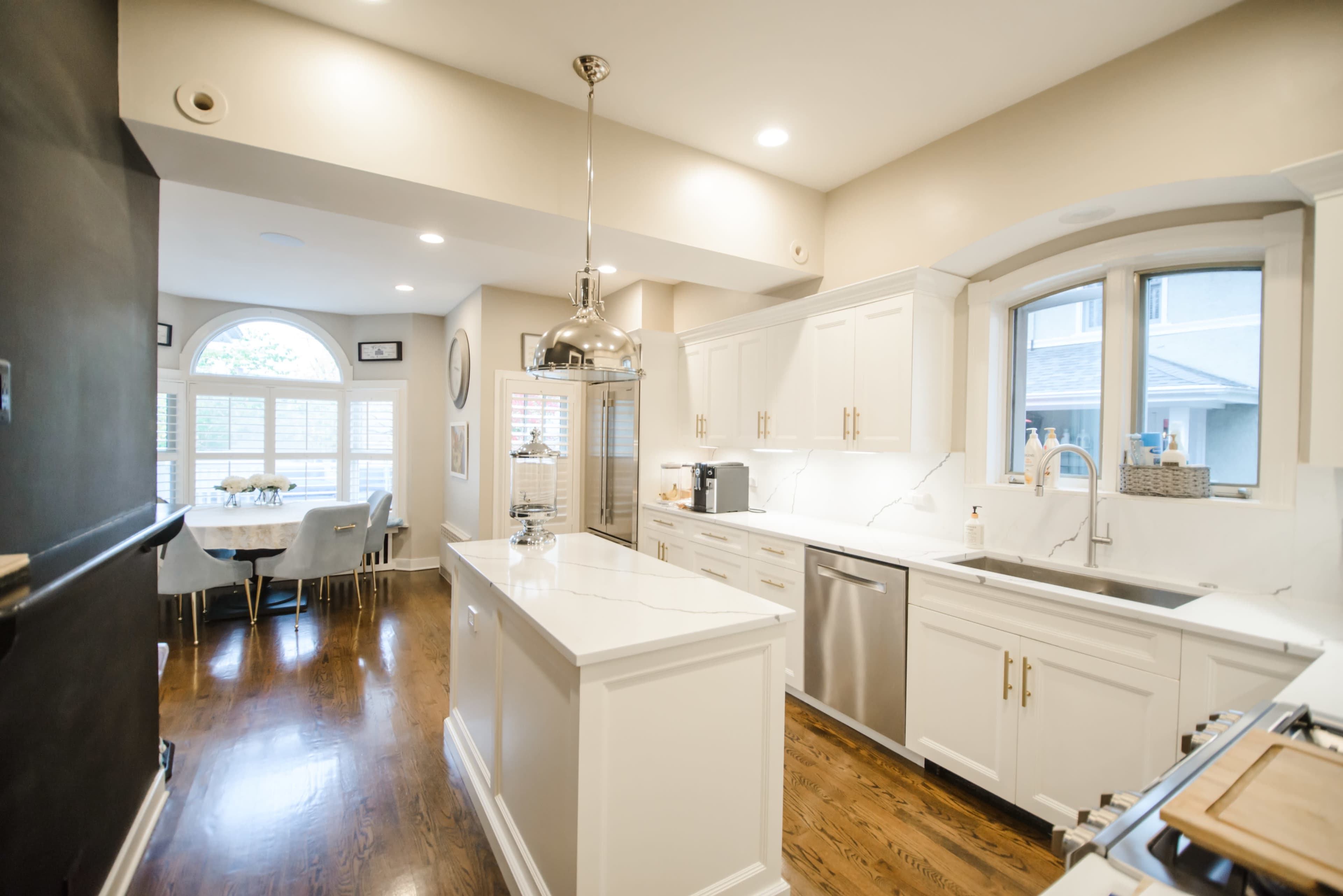 A modern kitchen features white cabinetry, a central island with bar seating, and stainless steel appliances, with a dining area visible through an archway.