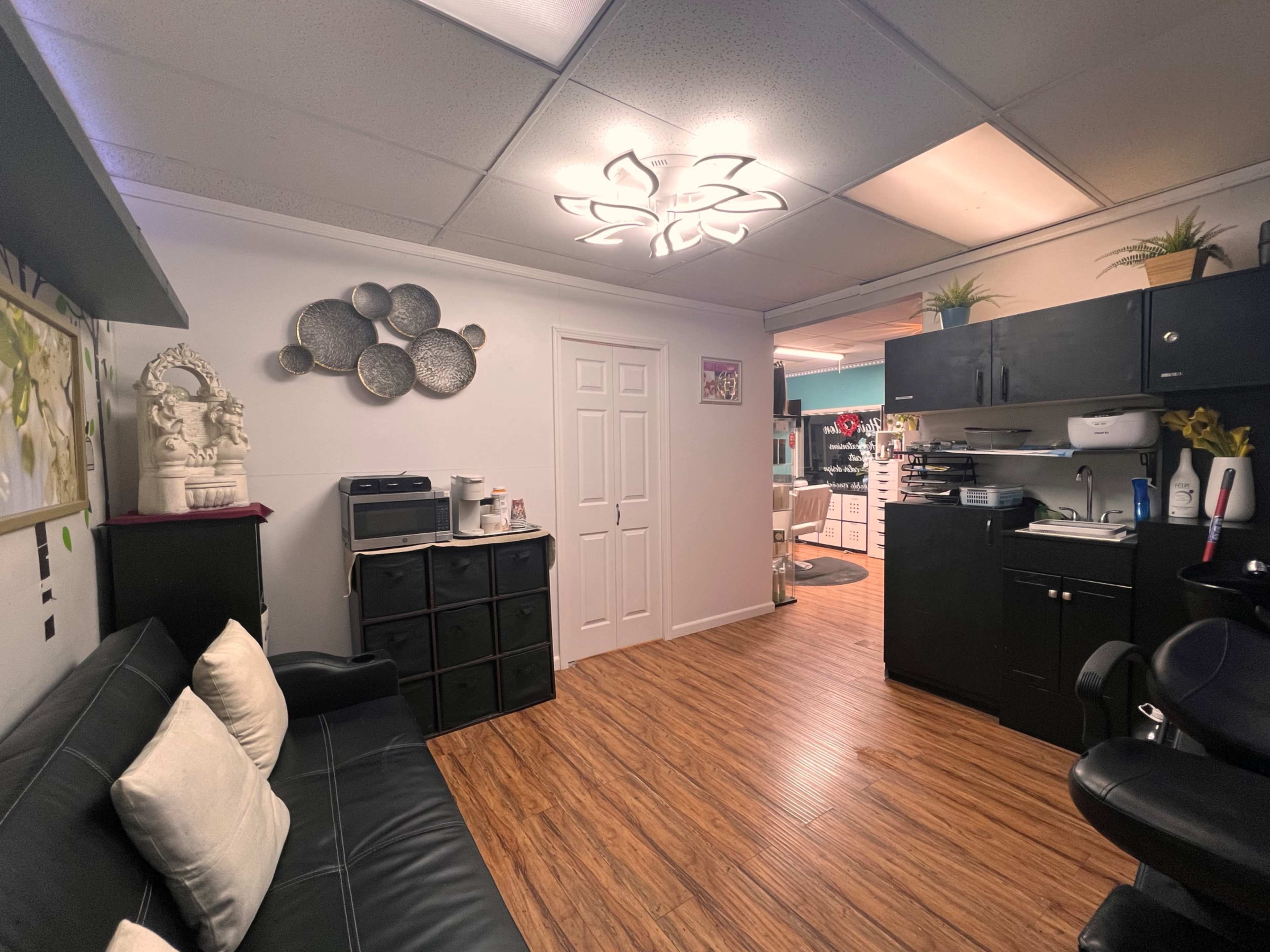 The image shows a well-organized office space with a black couch, a decorative wall featuring various round plates, and a workstation equipped with cabinets and a printer.
