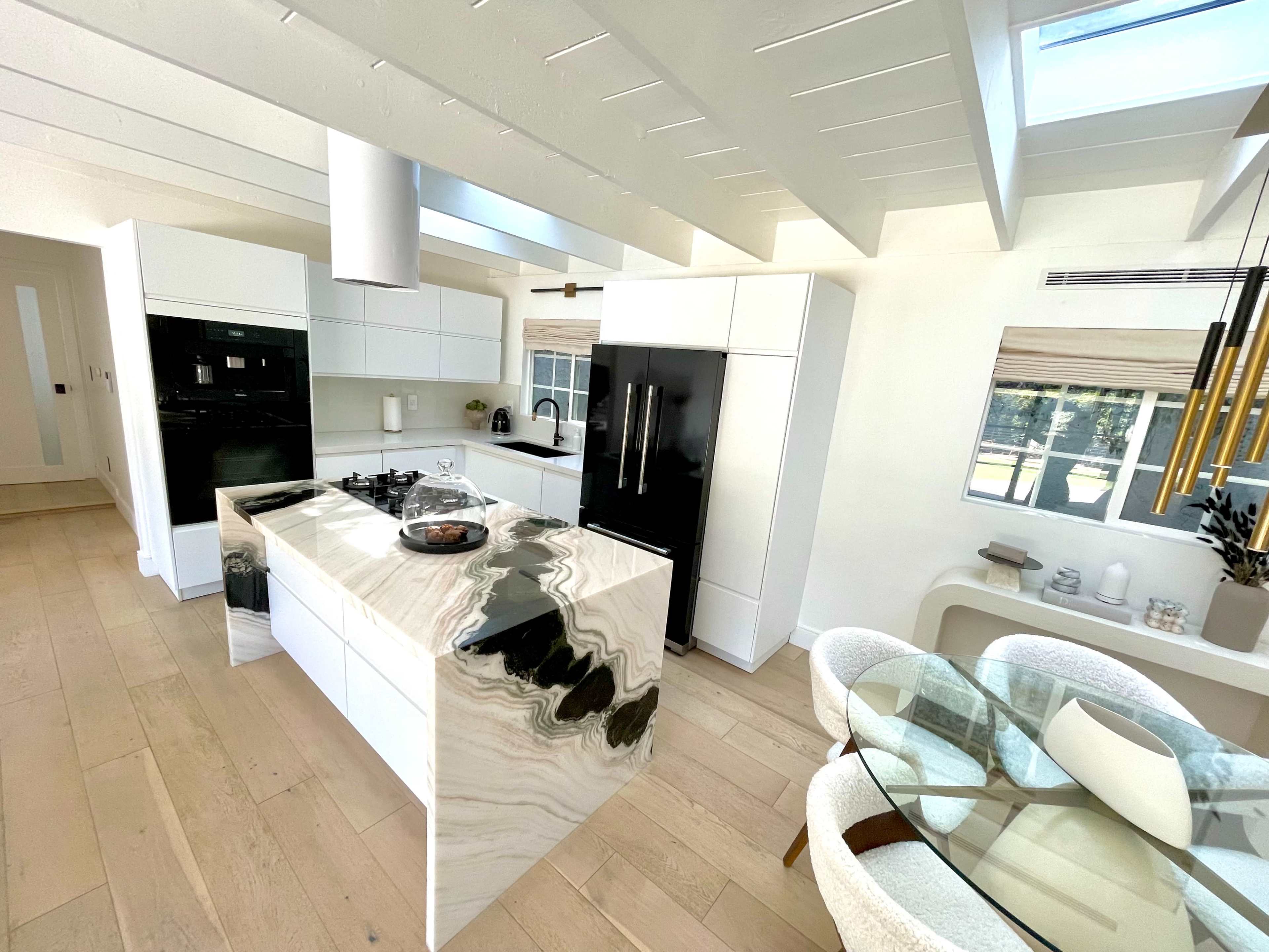 A modern kitchen featuring a marble island, black and white cabinetry, and a dining area with a circular table.