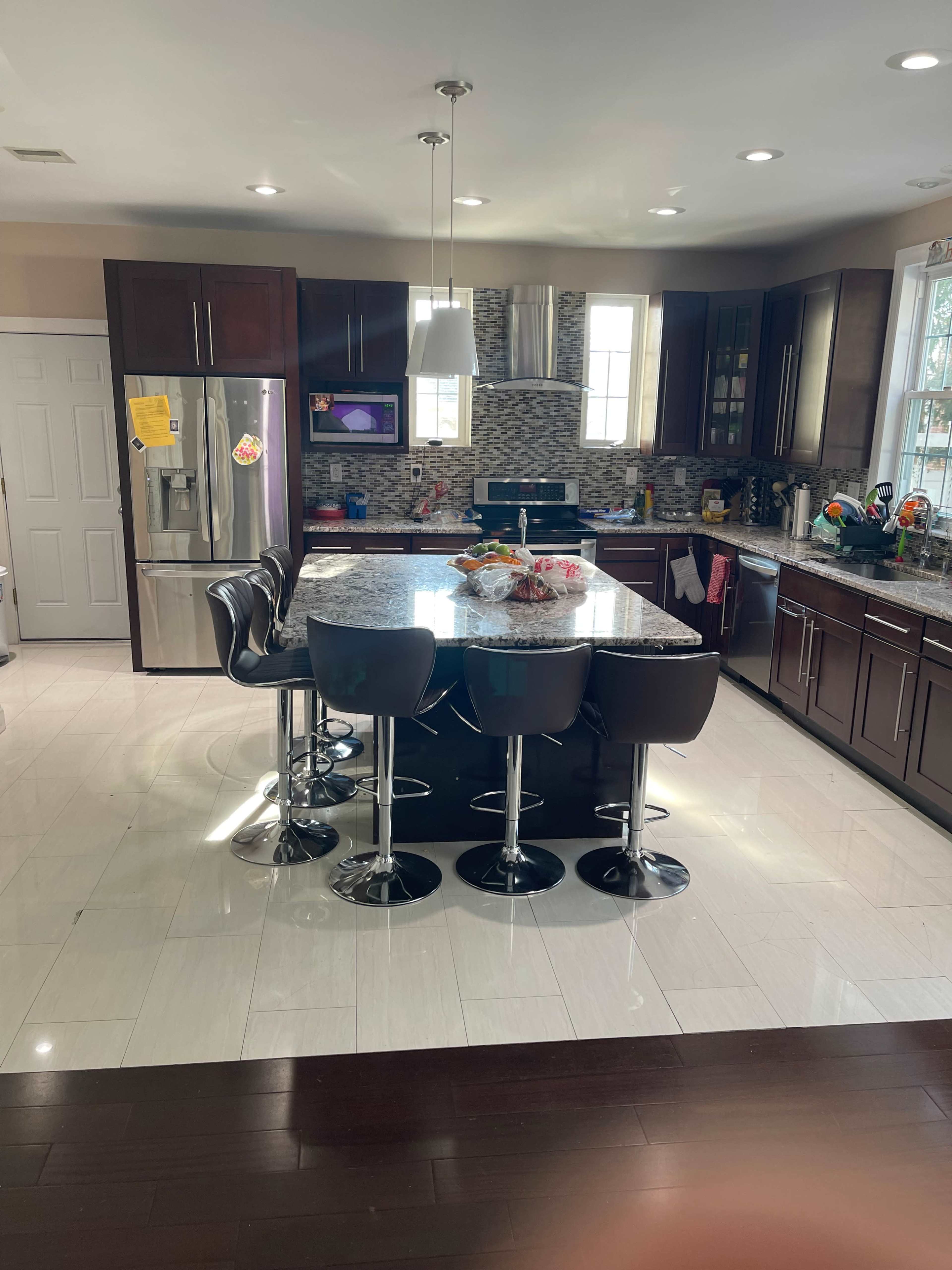 The image shows a modern kitchen with dark cabinetry, a large granite island with bar stools, and stainless steel appliances.