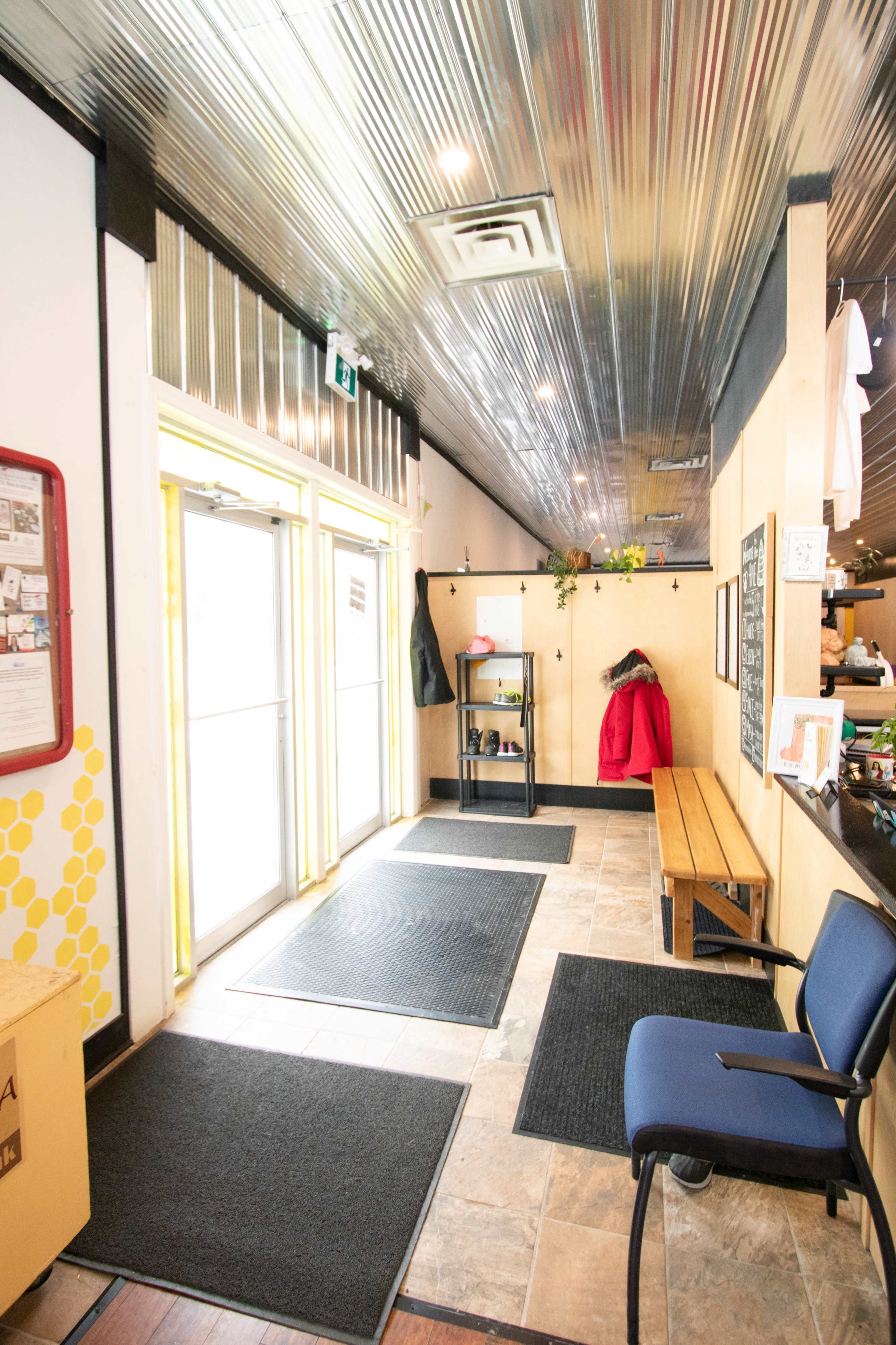 An entryway with a tiled floor, a bench, a blue chair, and double glass doors leading outside.
