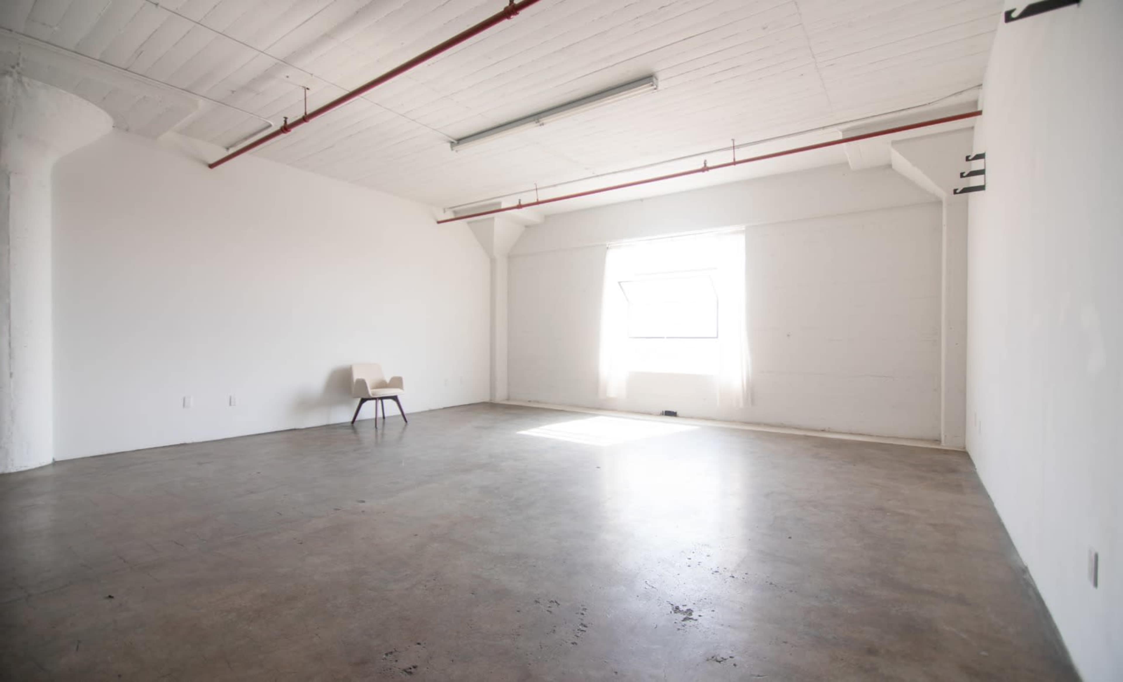 A minimalist, empty room with a single chair and a large window letting in natural light.