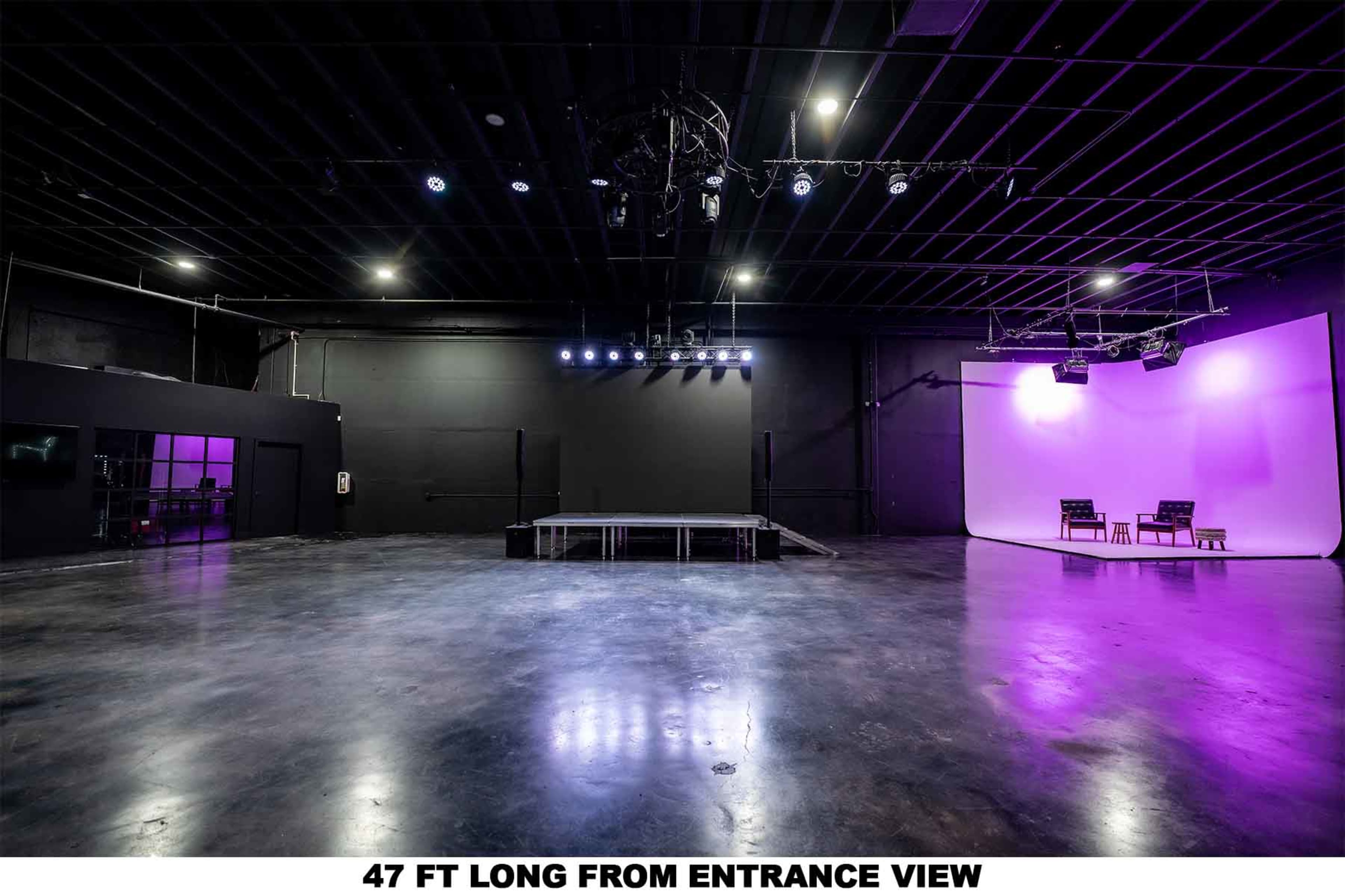 The image shows a large, empty stage area with a black ceiling and a white backdrop, illuminated by overhead lights.