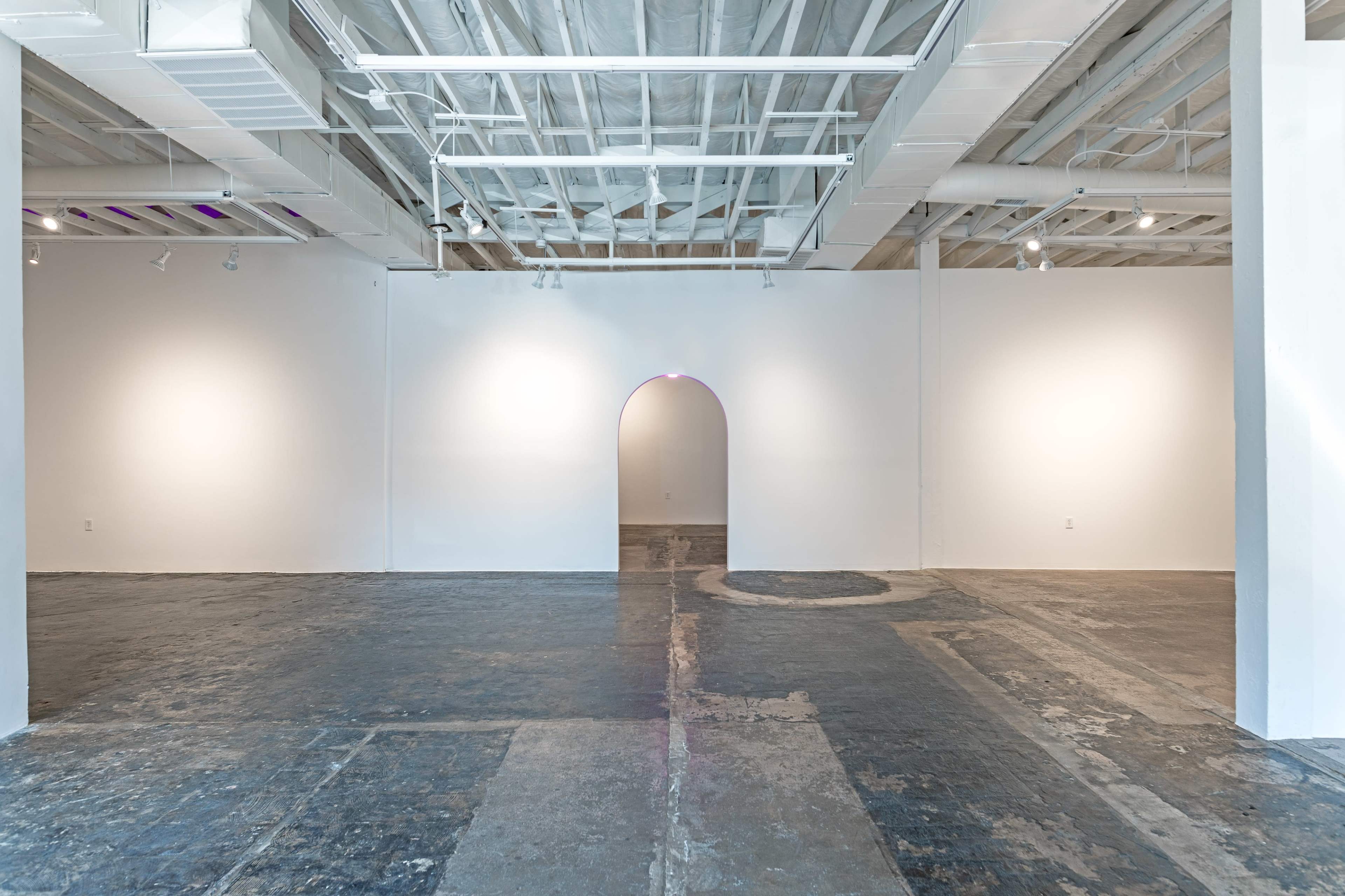 A spacious, empty art gallery with white walls and a curved archway leading to a darker area.