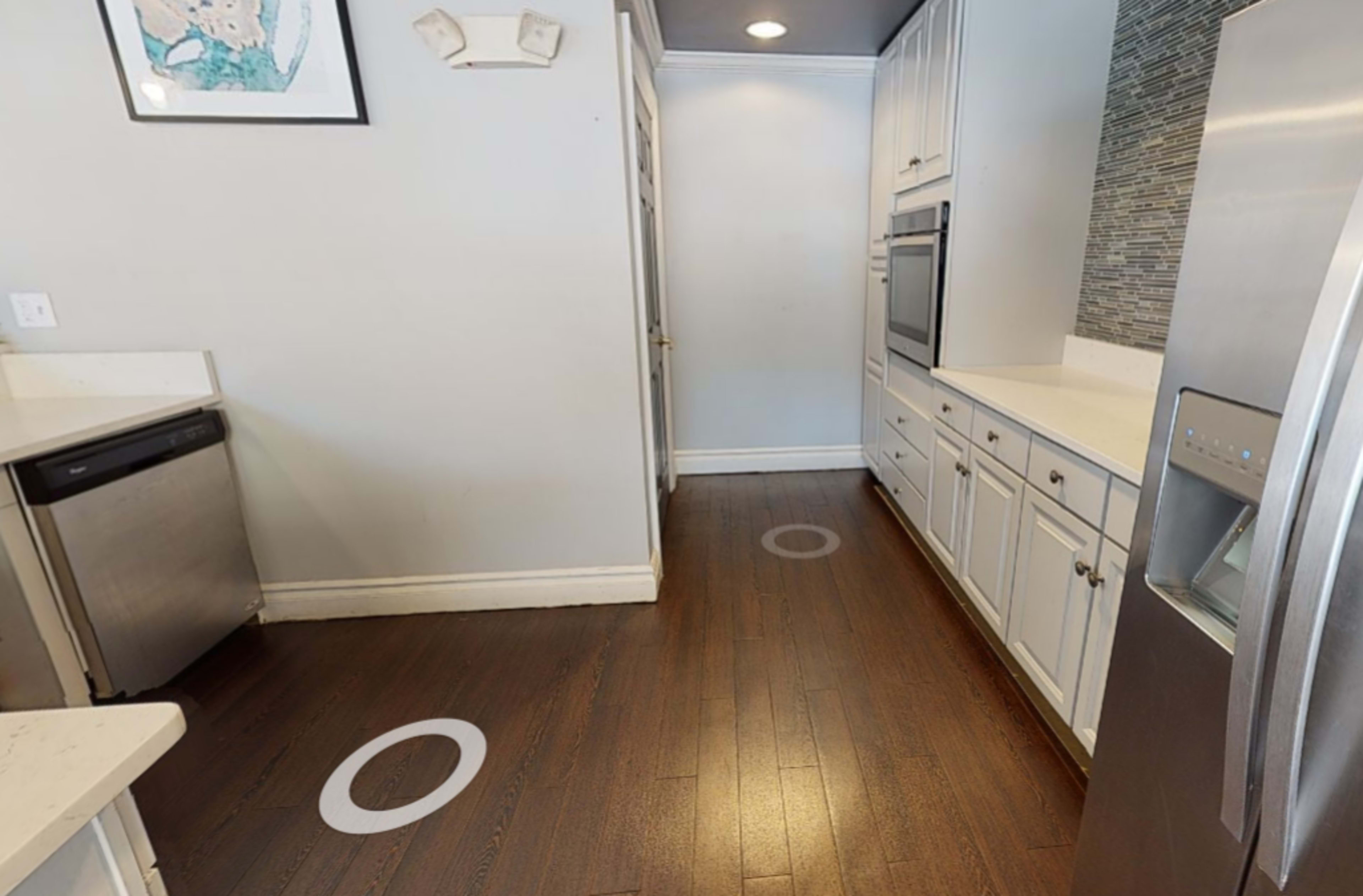 A modern kitchen features stainless steel appliances, white cabinetry, and circular floor markings on a hardwood floor.