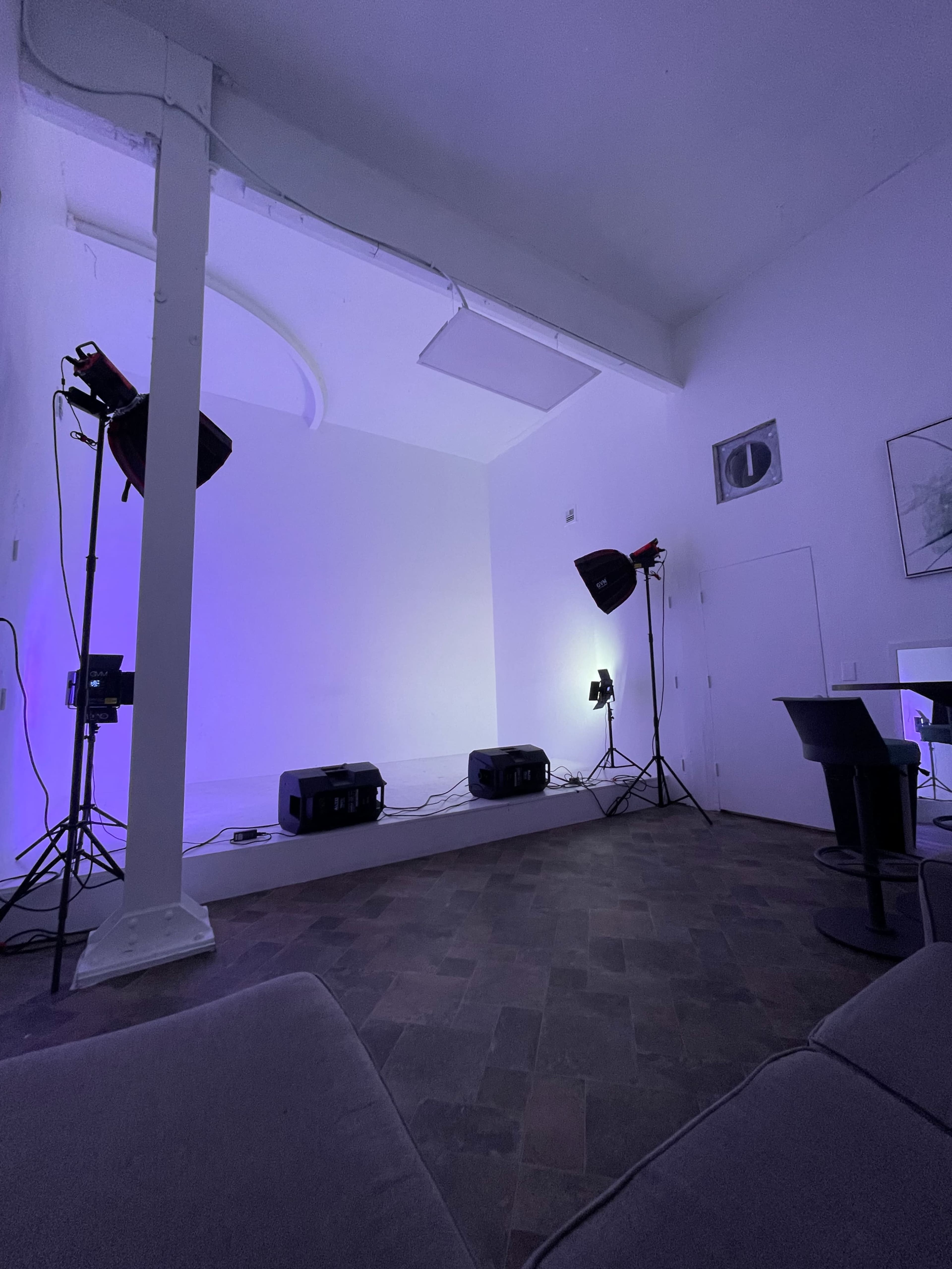 The image shows a spacious, well-lit studio with purple lighting, three studio lights on poles, and a black table set against a white backdrop.
