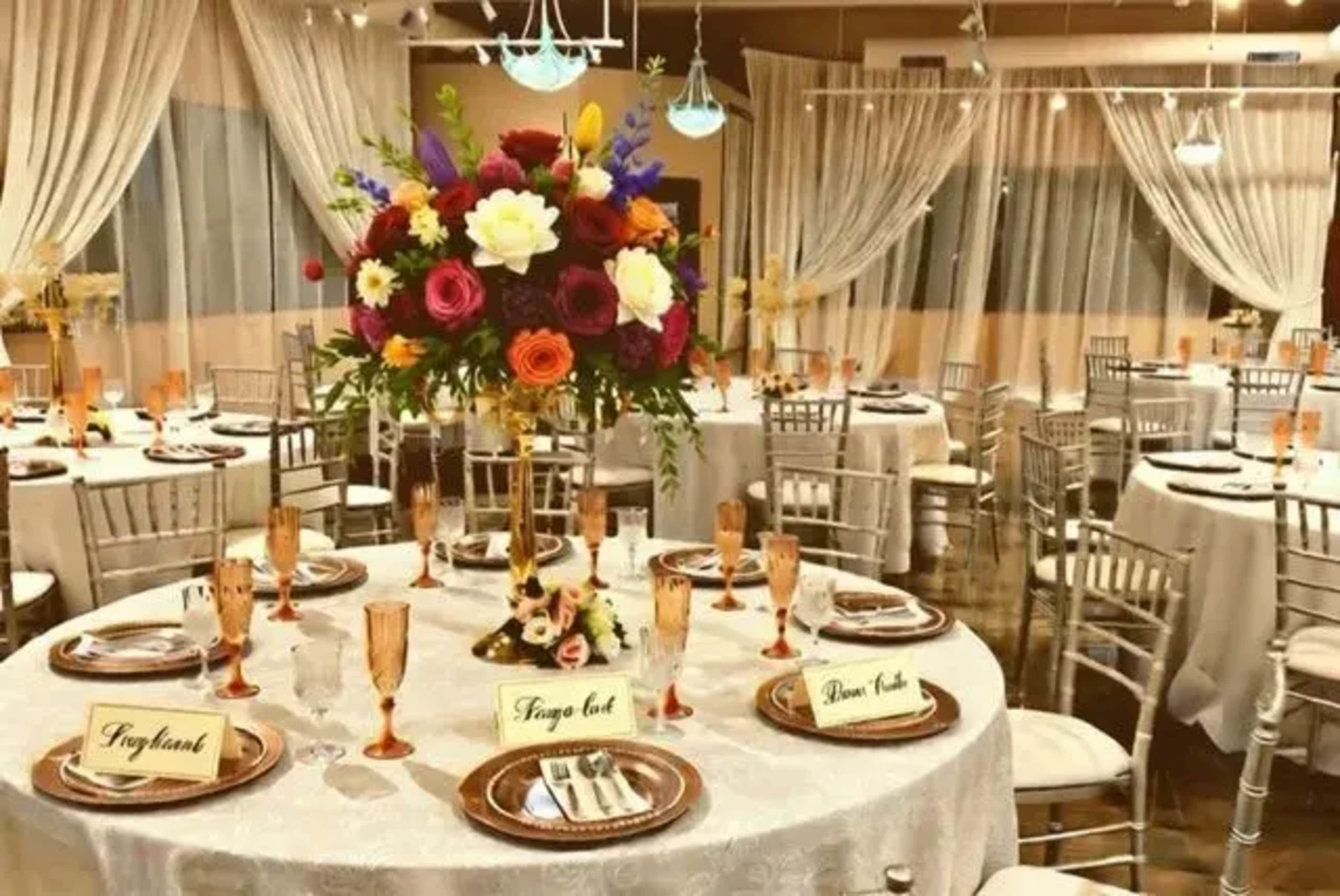 The image shows an elegantly arranged dining room with round tables set for a formal event, featuring floral centerpieces and place settings.