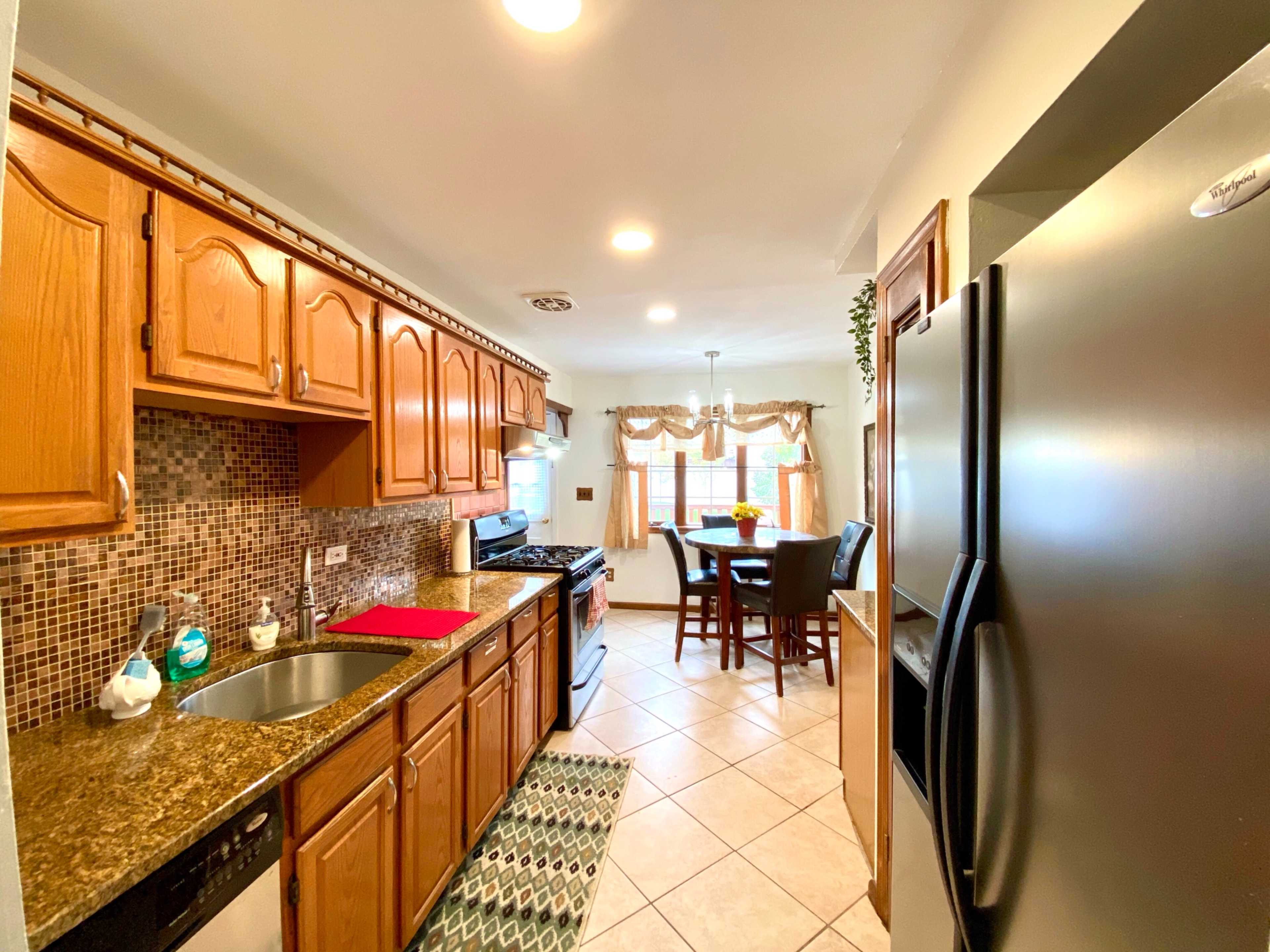 A kitchen features wooden cabinets, a granite countertop, a gas stove, a sink, and a dining table with chairs.
