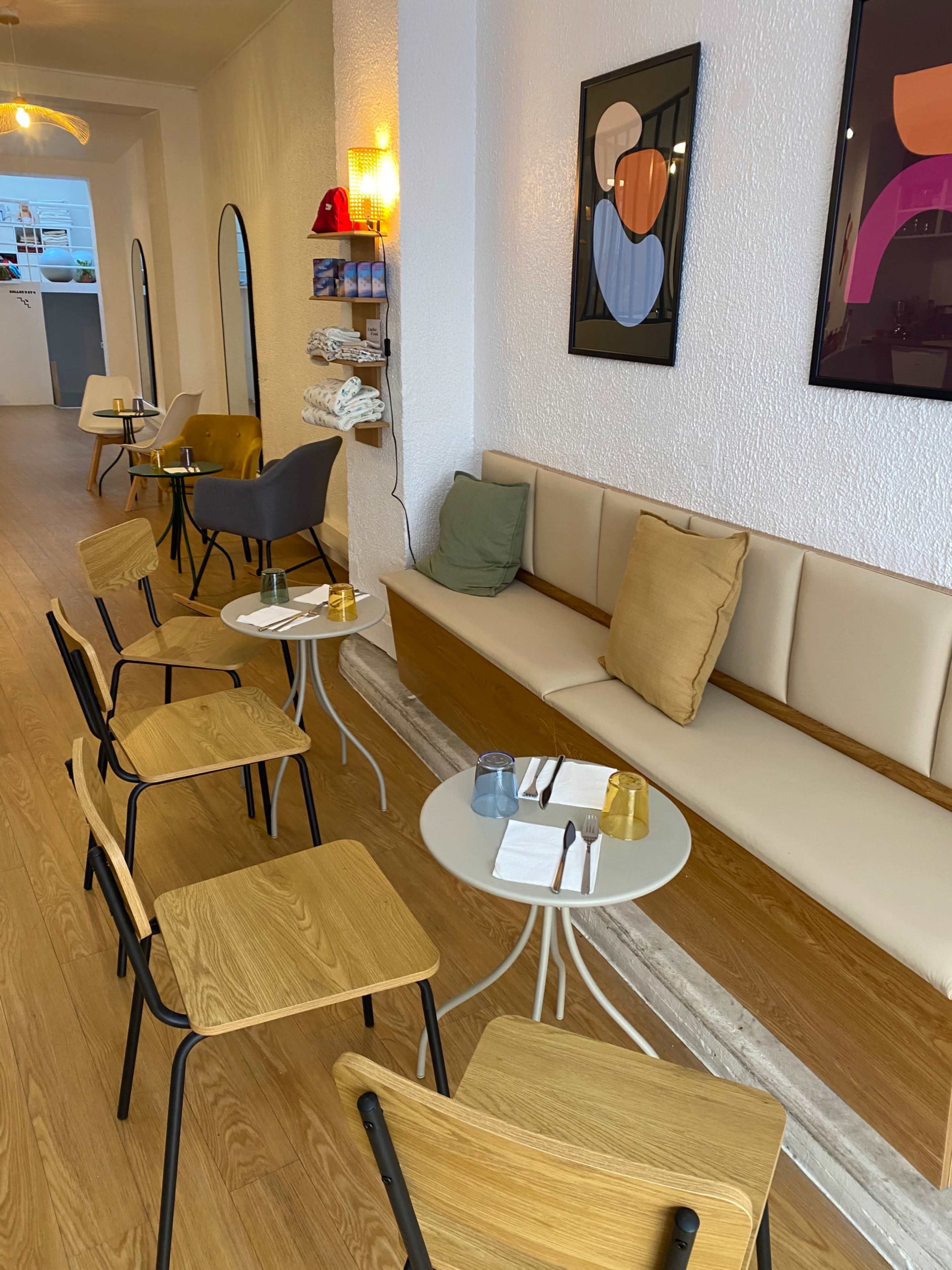The image shows a modern café interior with wooden seating, small round tables, and artistic wall decorations.