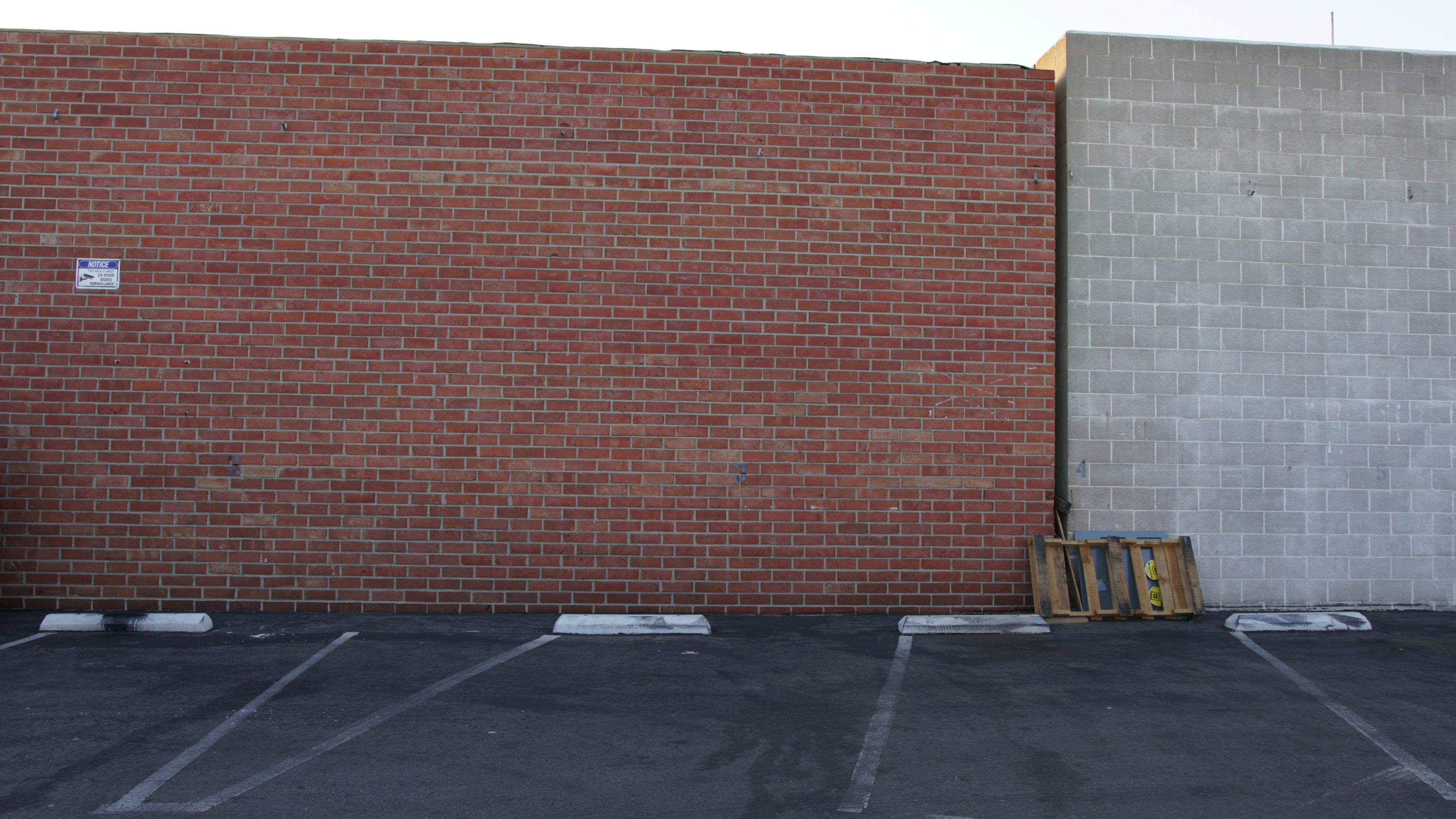 A parking lot with empty spaces beside a red brick wall and a gray concrete wall.