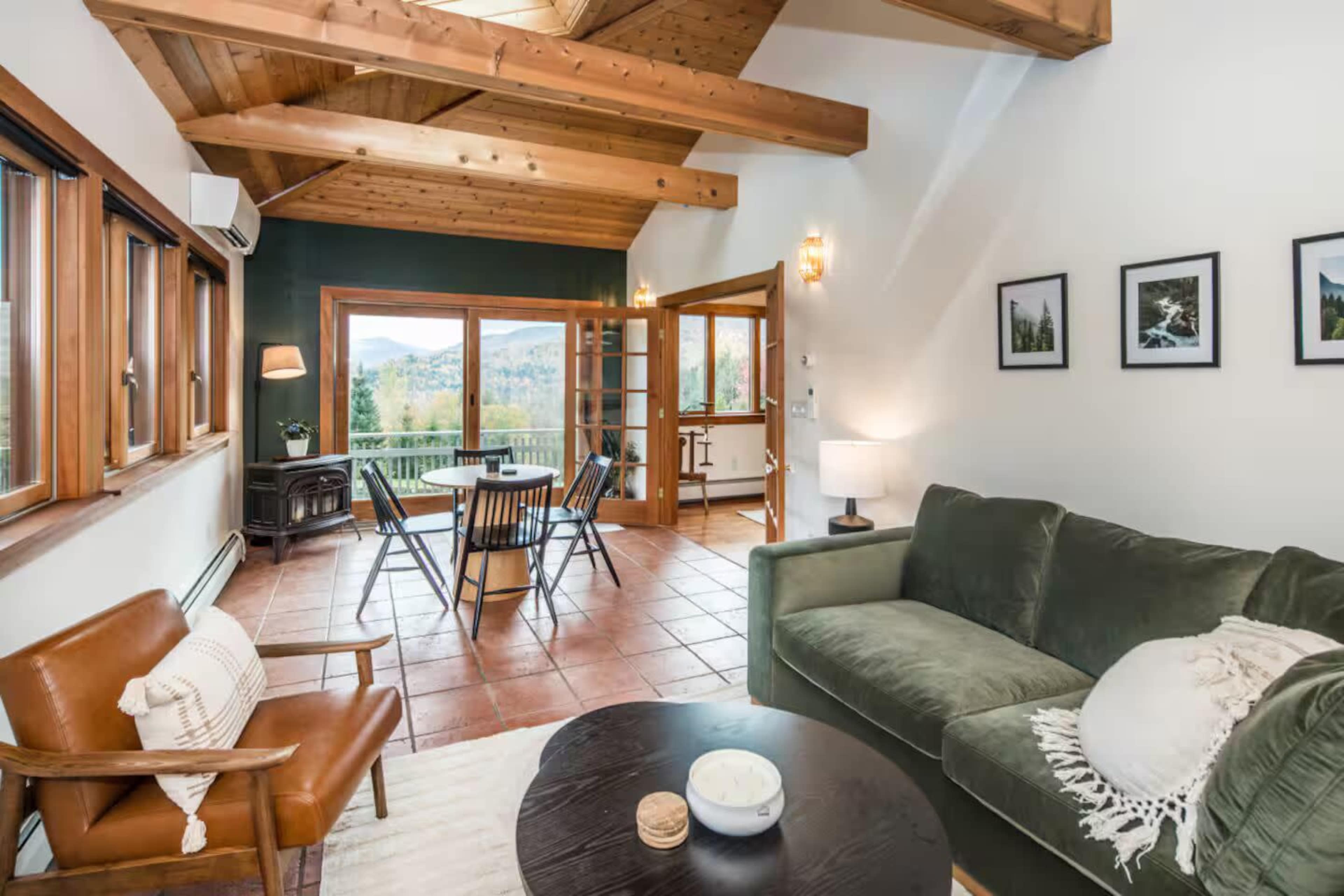 The image shows a cozy living room with a green sofa, a wooden coffee table, and large windows that open to a scenic view.