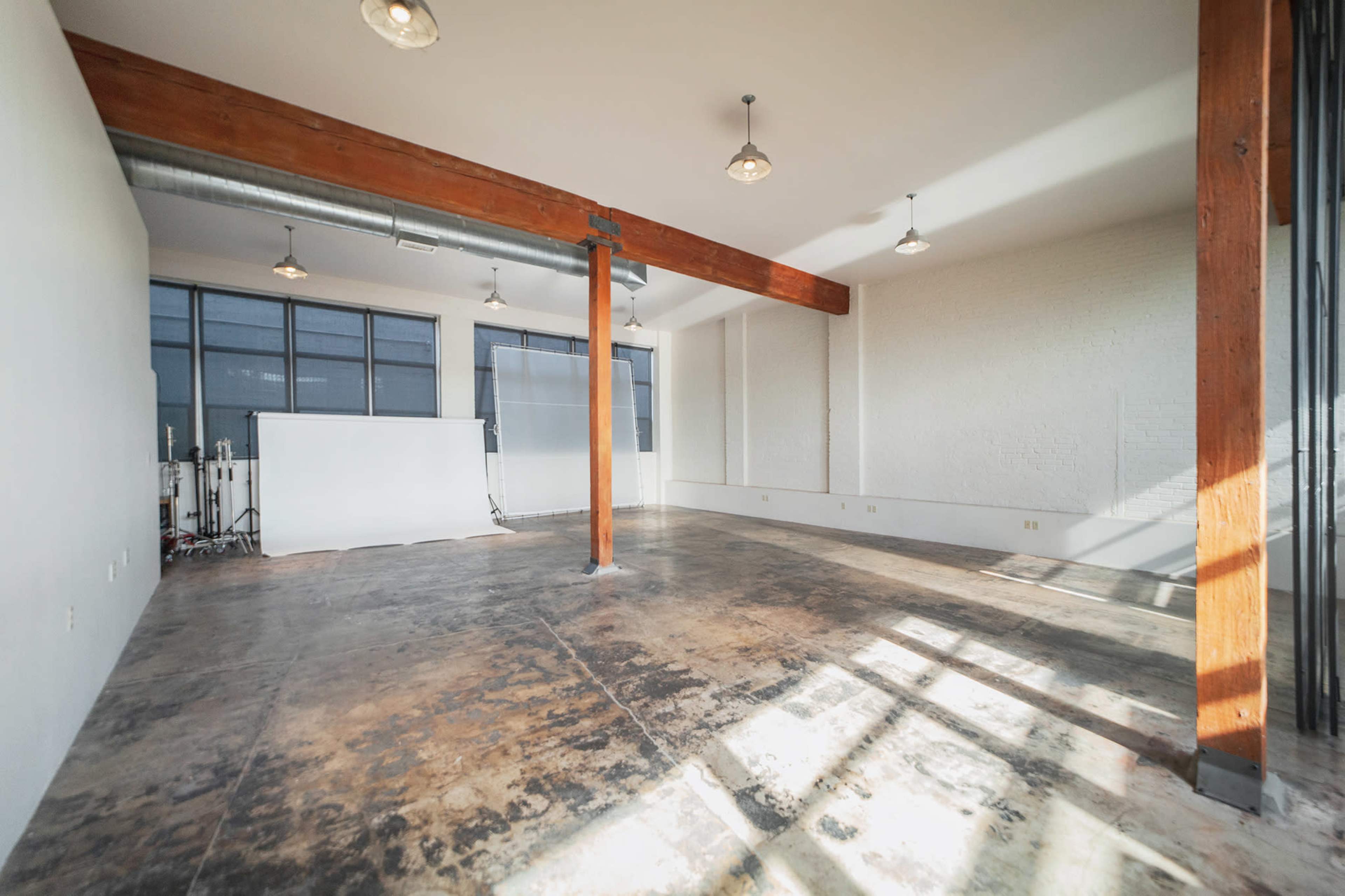 A spacious, empty room with concrete floors, large windows, and exposed wooden beams.