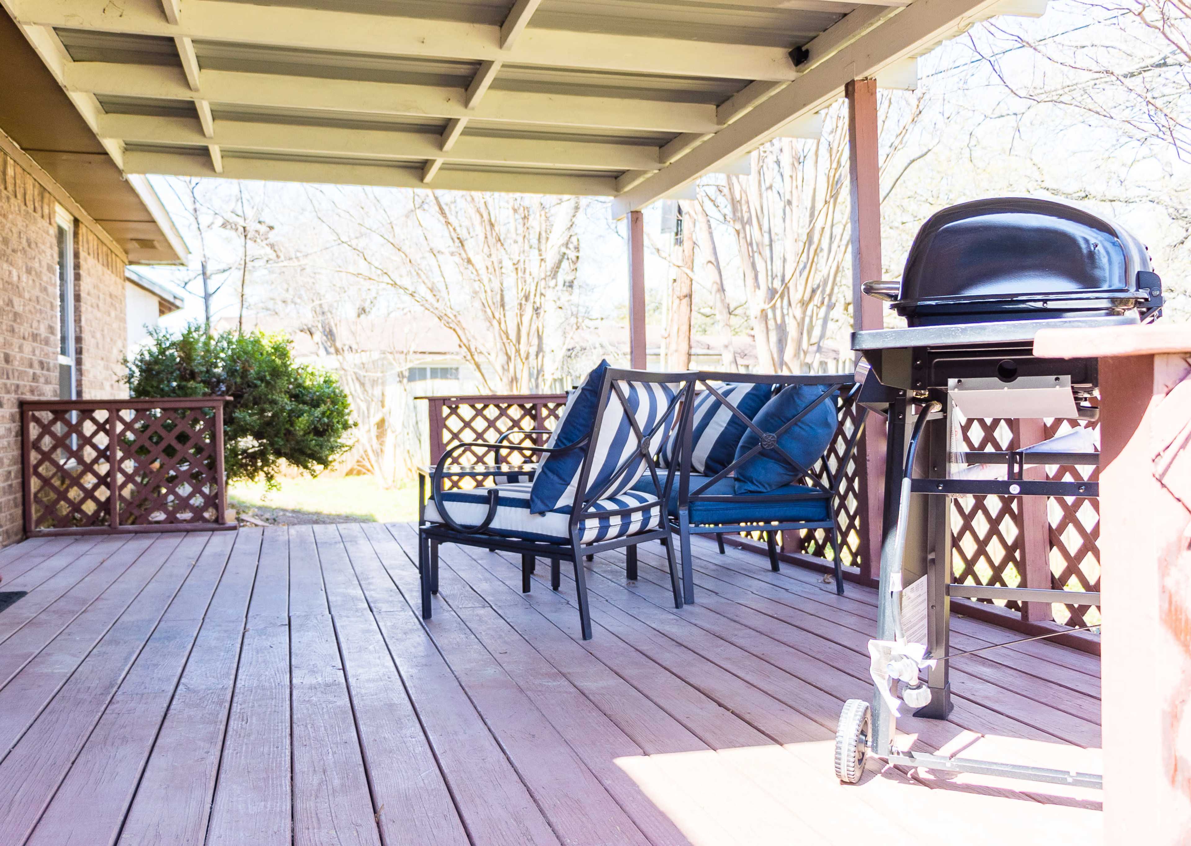 A deck area with two blue chairs, a black grill, and a shaded overhang.