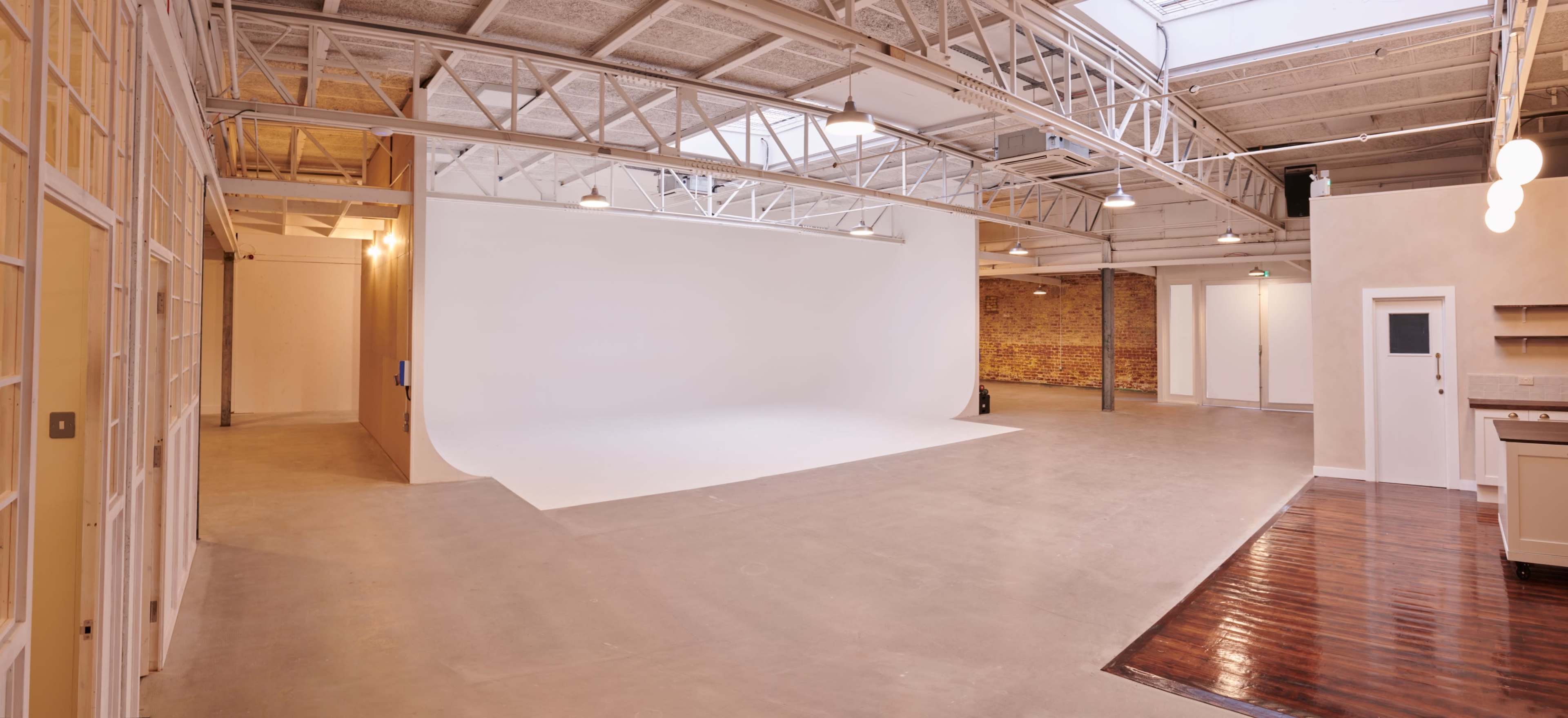 The image shows a spacious indoor studio with a white backdrop, exposed brick walls, and large windows allowing natural light.