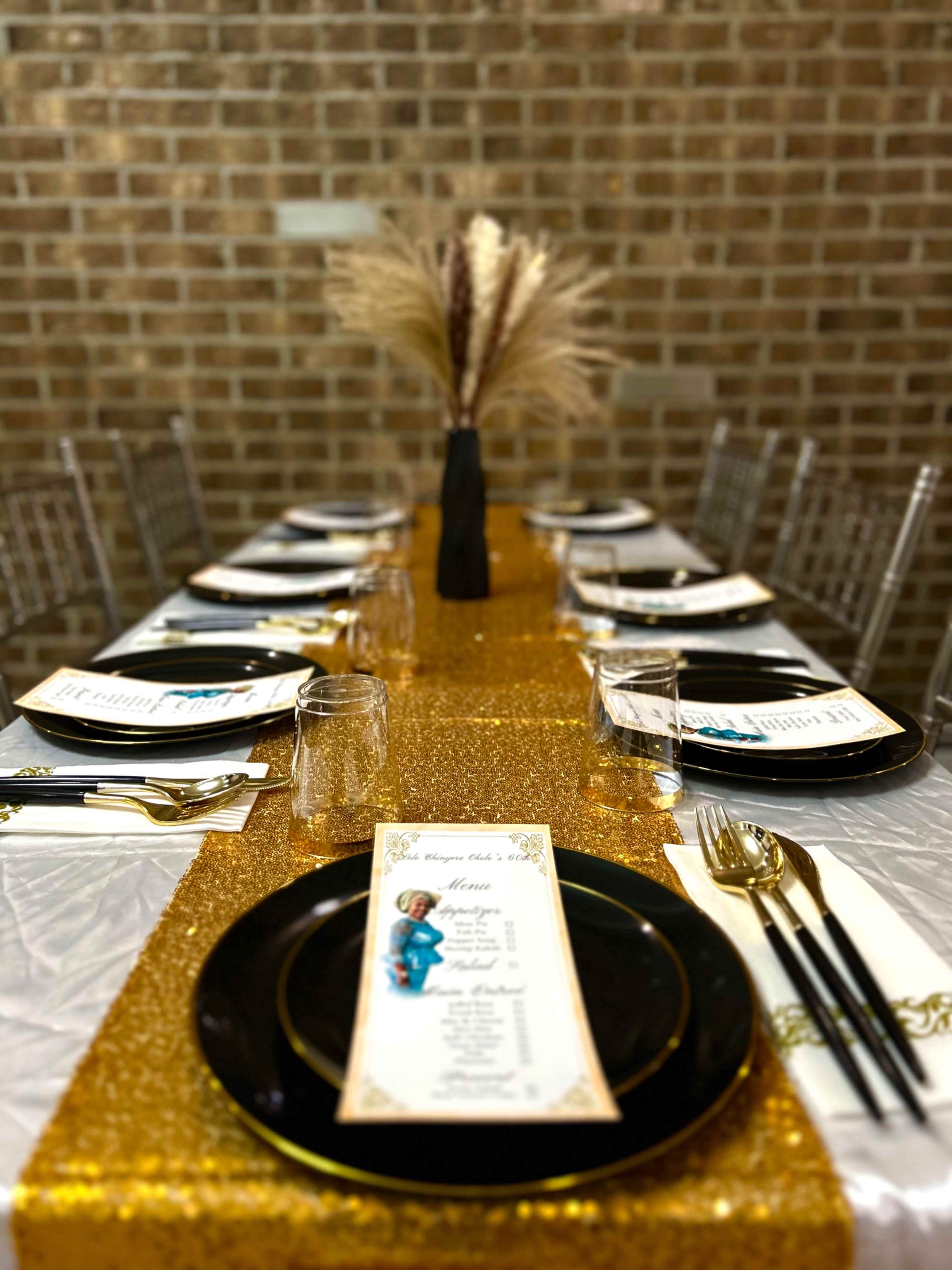 A neatly set dining table features gold and black tableware with a decorative vase and menu cards.