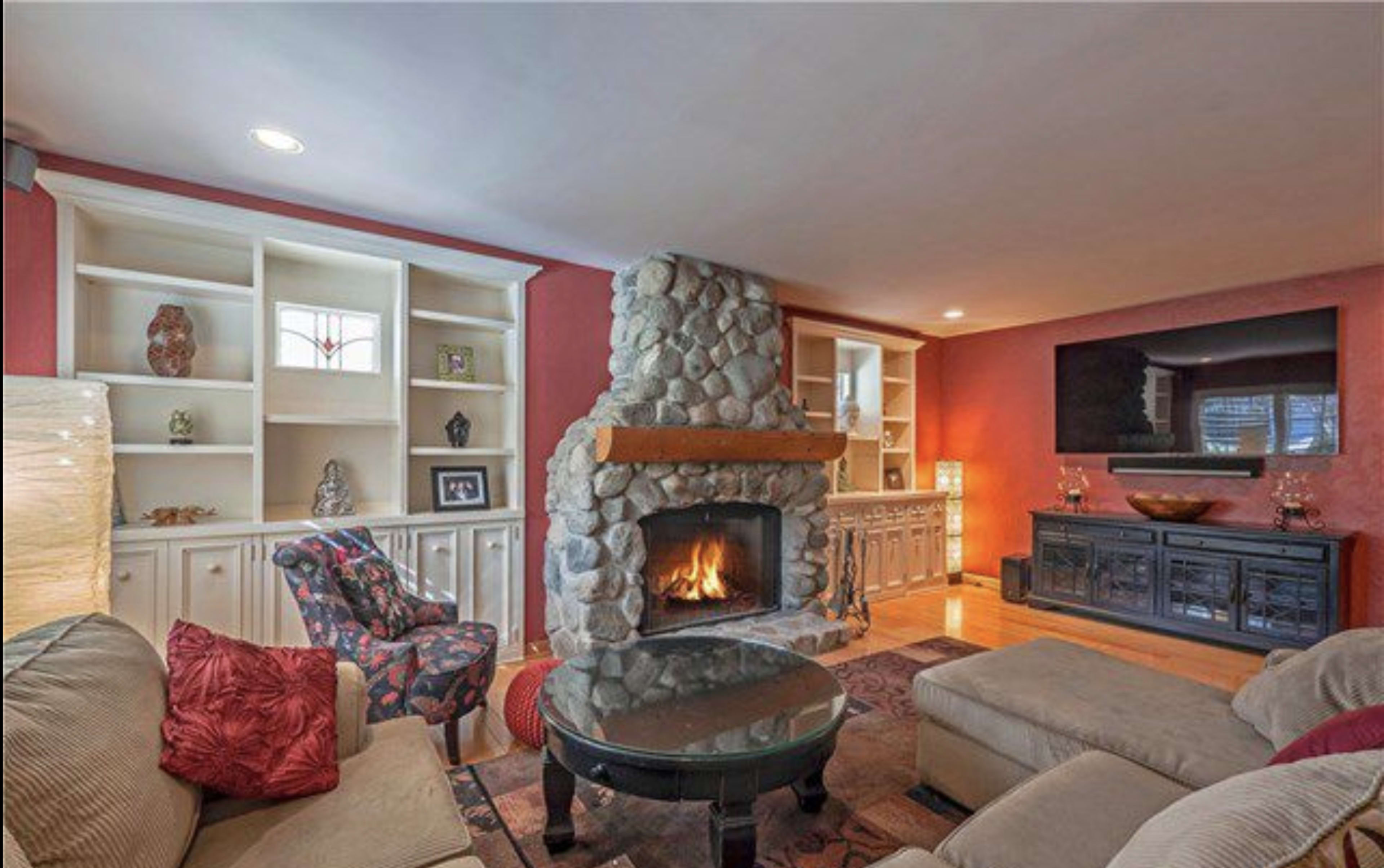 The living room features a stone fireplace, built-in shelves, and a large television mounted on the wall.