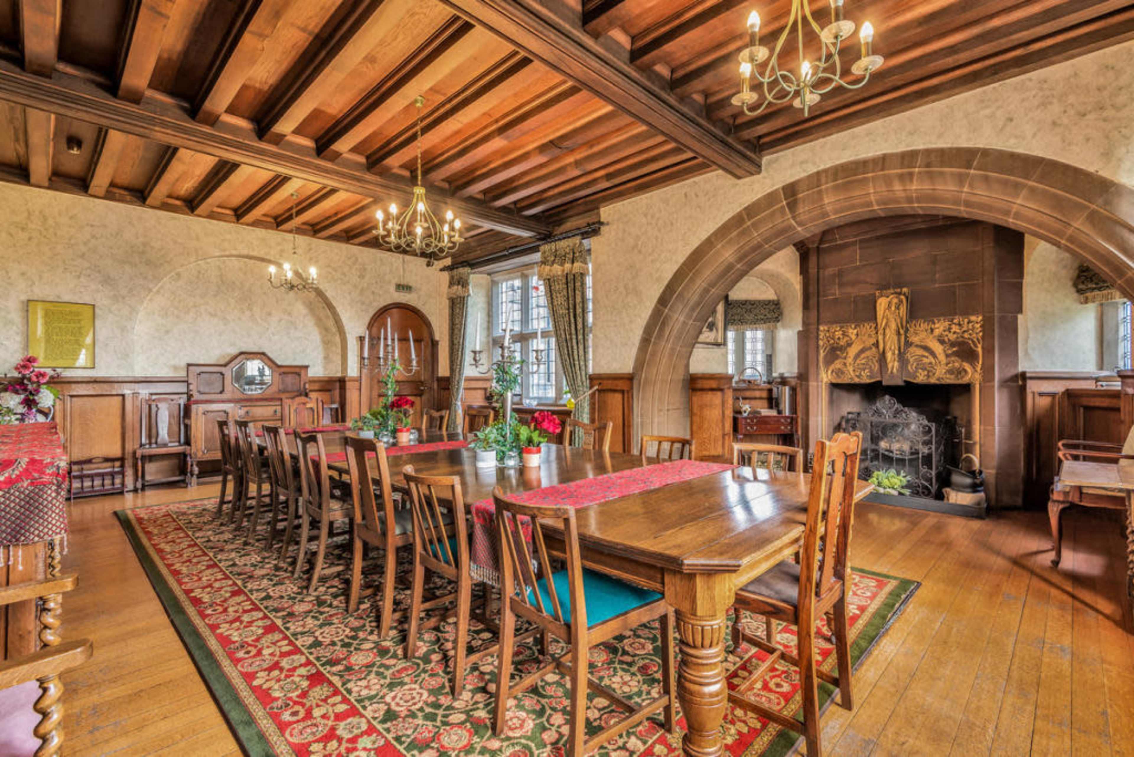A spacious dining room featuring a long wooden table surrounded by chairs, a decorative fireplace, and large windows with curtains.