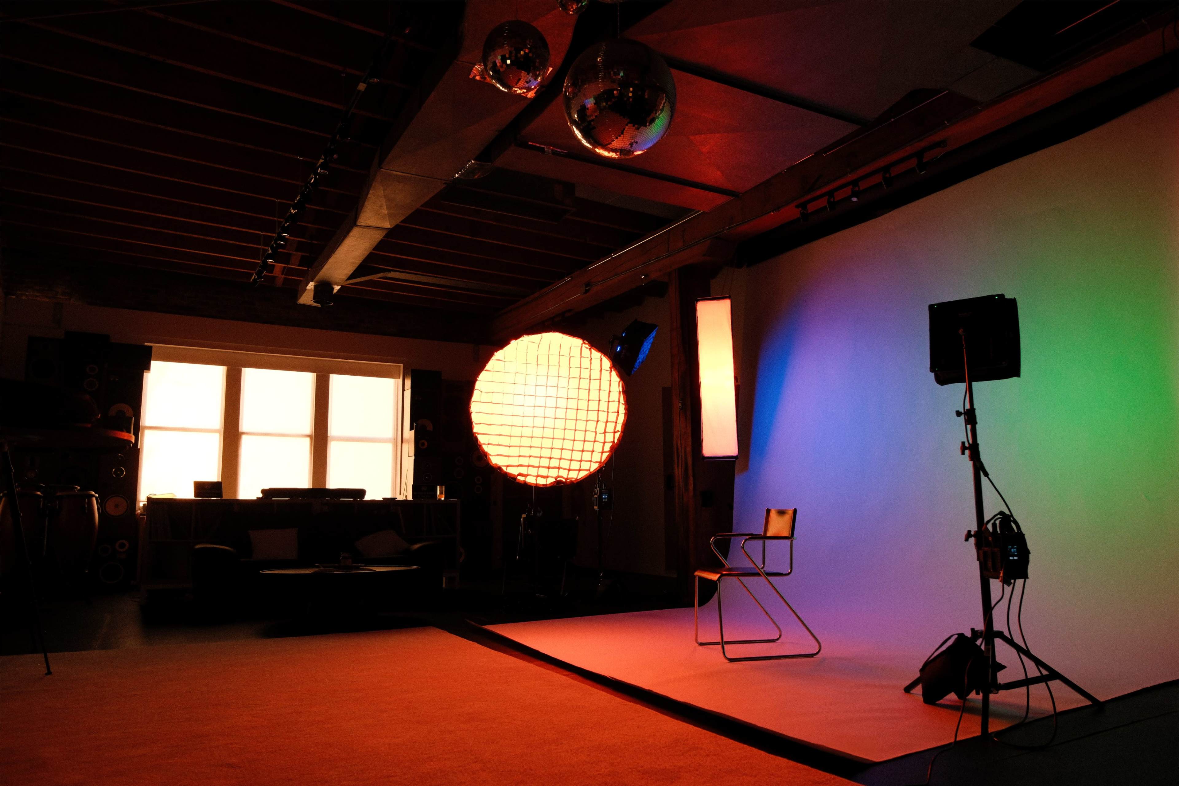 The image shows a photo studio with a chair in front of a colorful backdrop, illuminated by various lights and featuring a large round lamp and disco balls.