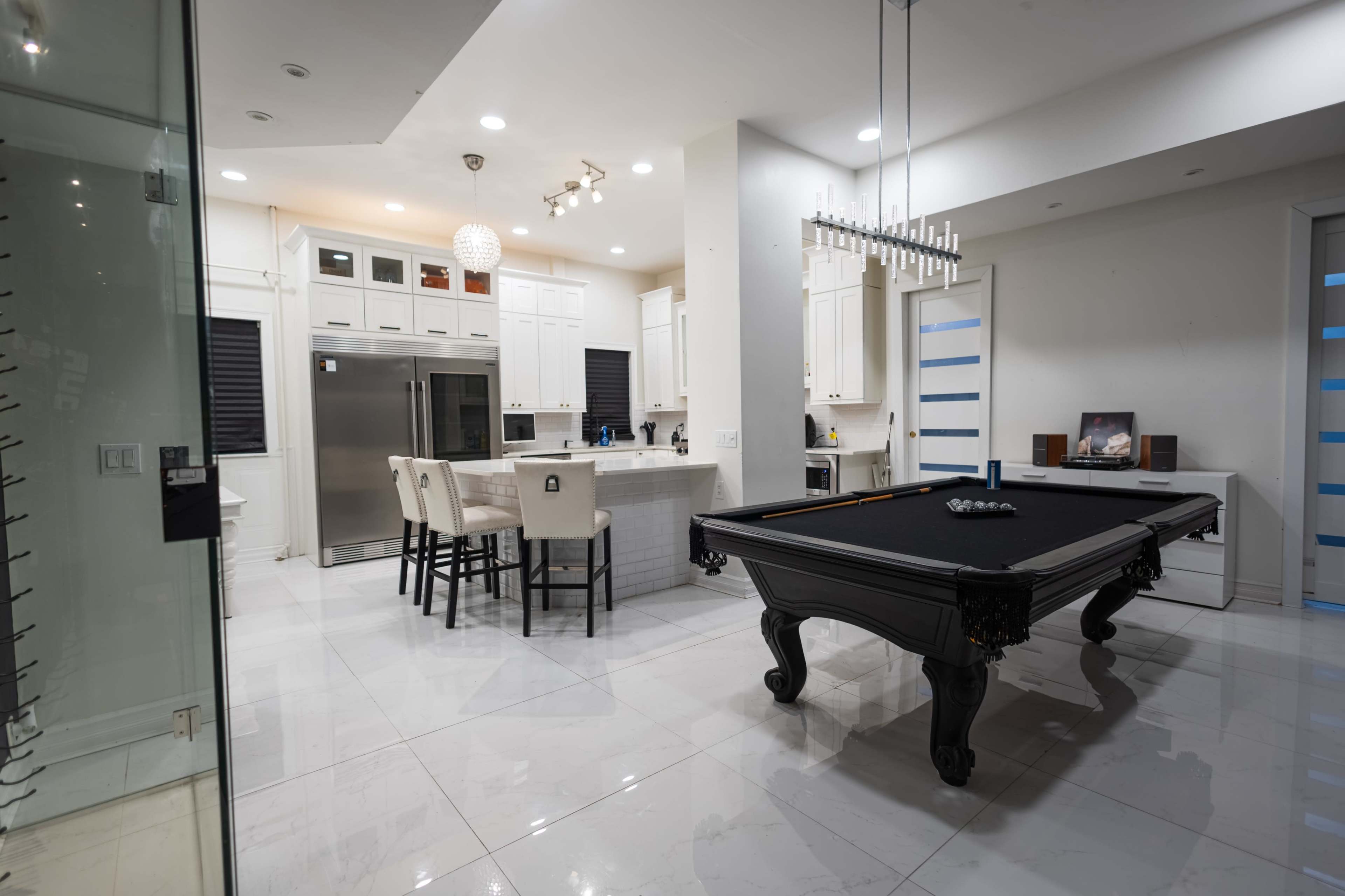 The image shows a modern kitchen with white cabinetry and a black billiard table in the foreground.