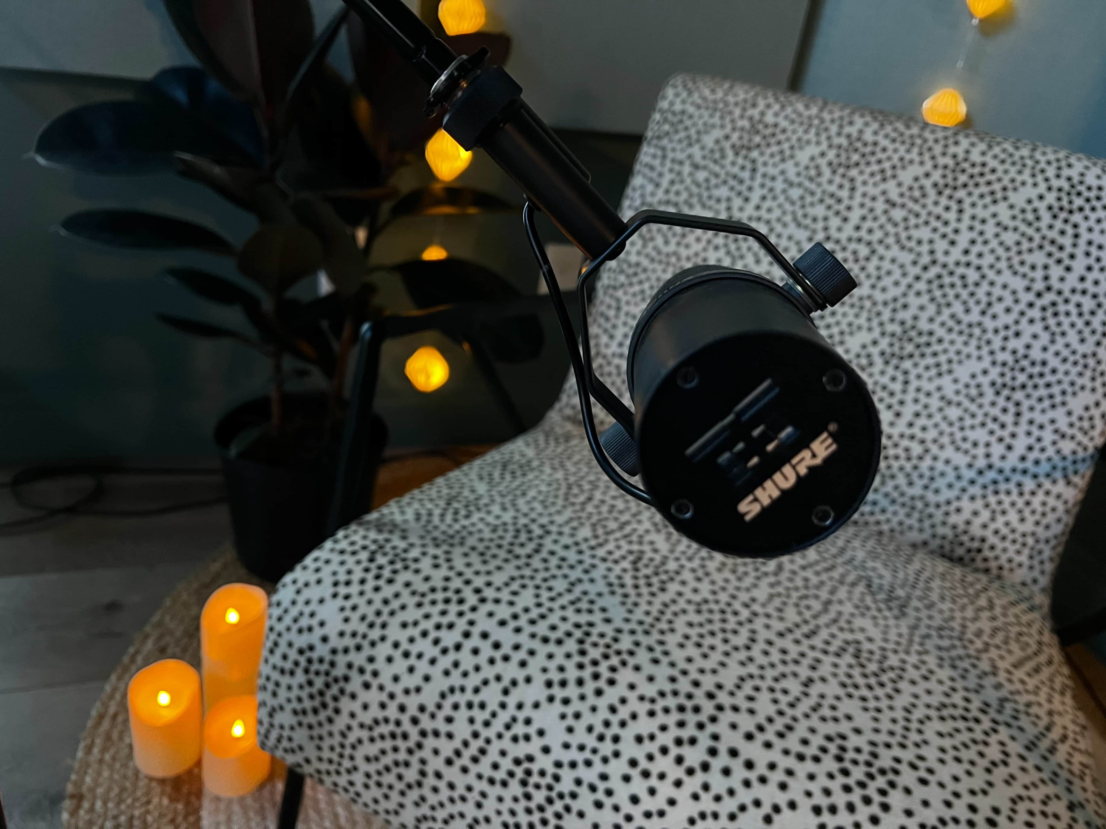 A black microphone is positioned close to a patterned chair, surrounded by softly glowing candles and a plant in the background.