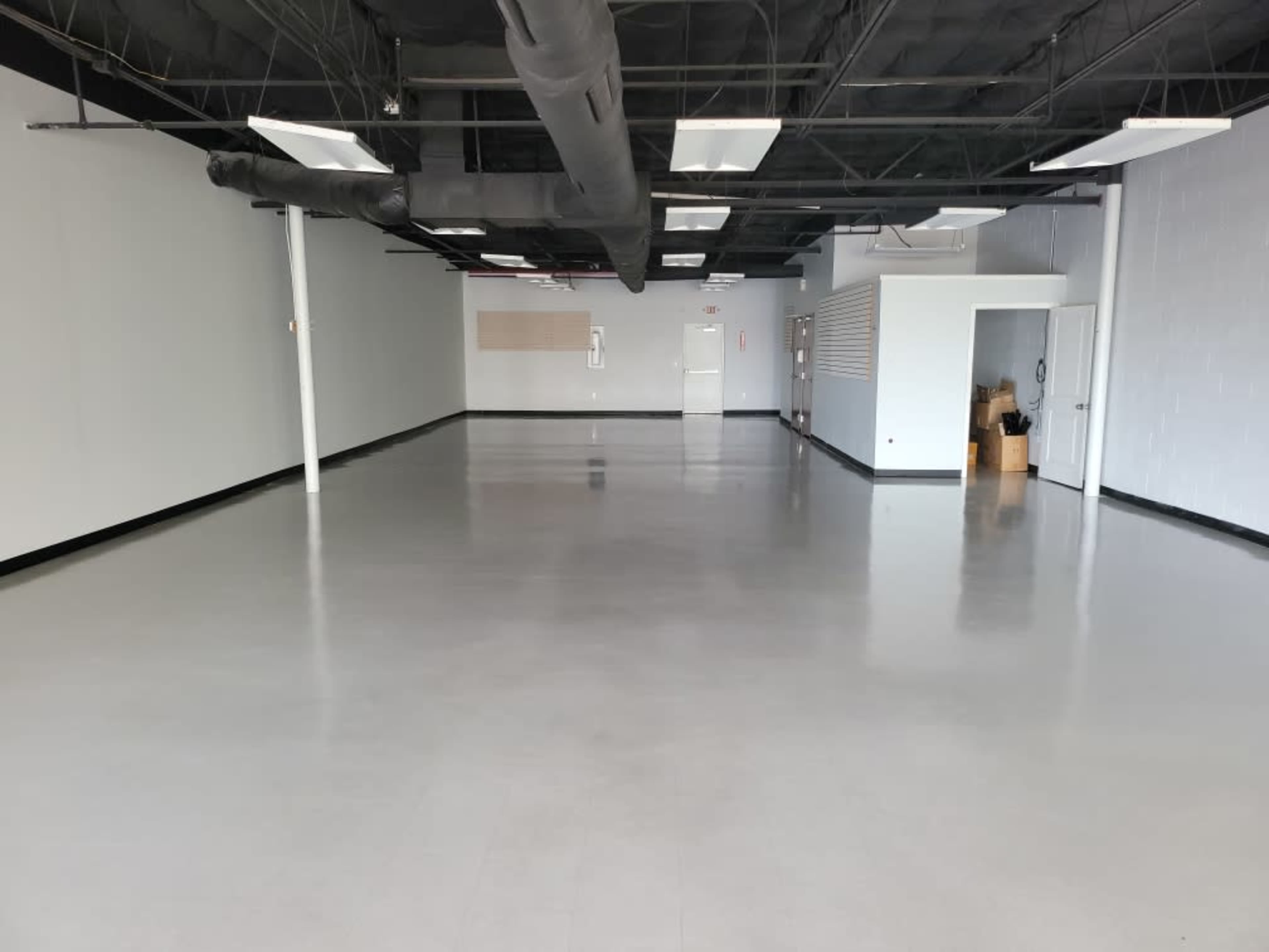 A spacious, empty commercial interior with gray walls, a polished floor, and a door at the far end.