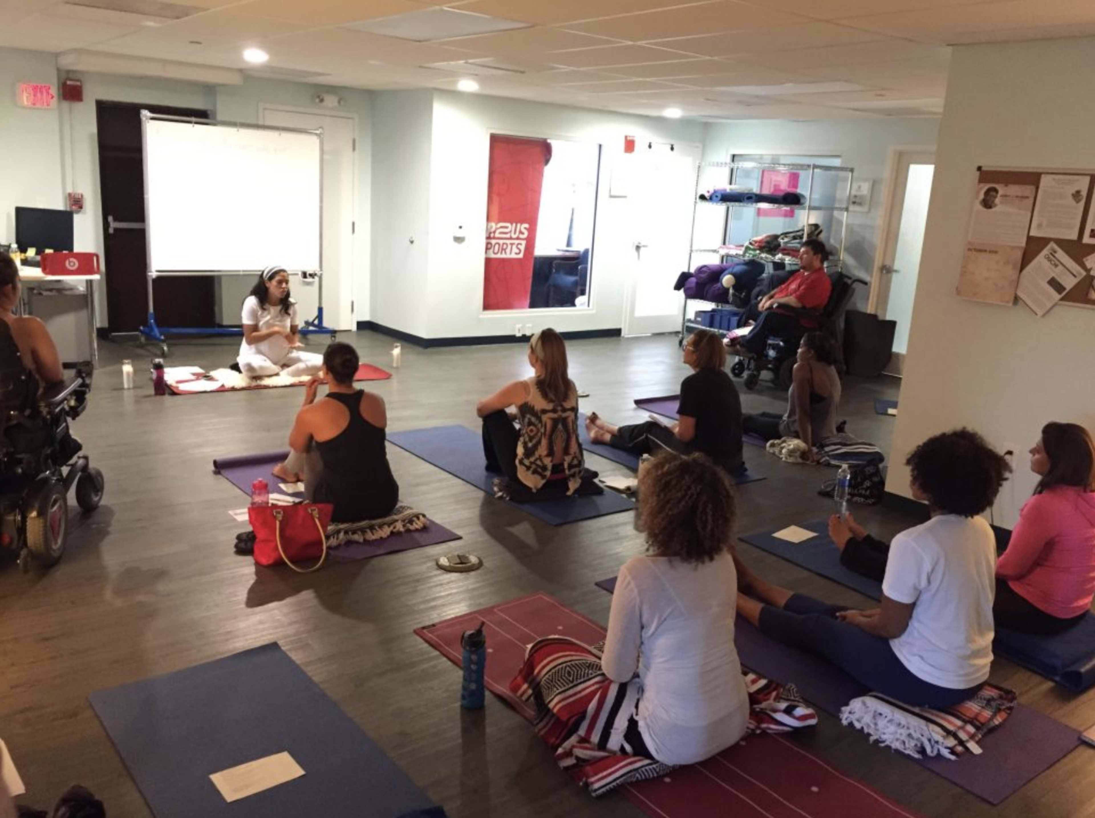 A group of people participates in a yoga class led by an instructor in a spacious room equipped with yoga mats and various workout gear.