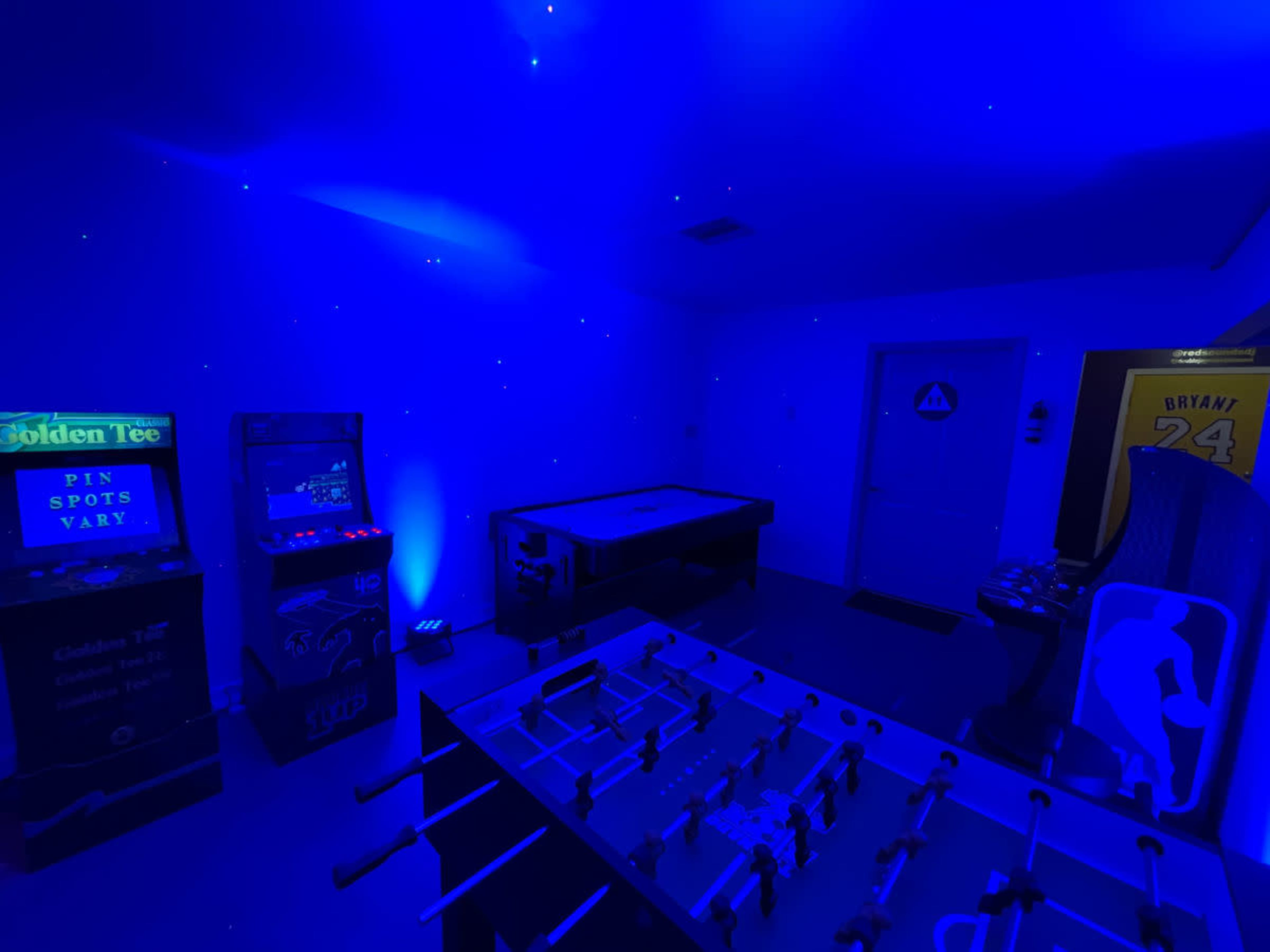 The room features a blue-lit game area with a foosball table, a pool table, and two arcade machines.