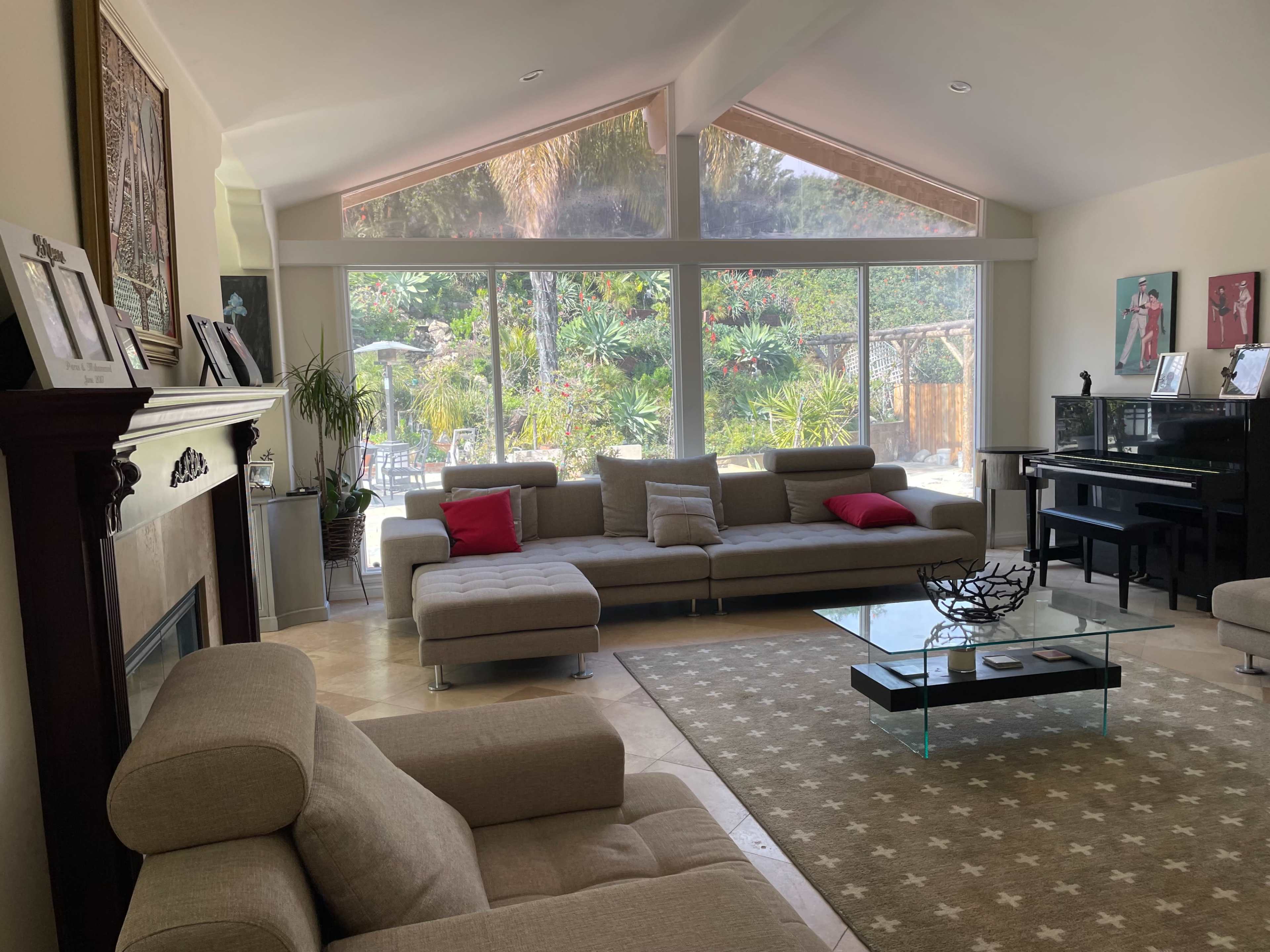 A spacious living room features a large sectional sofa, a glass coffee table, and large windows that overlook a landscaped garden.