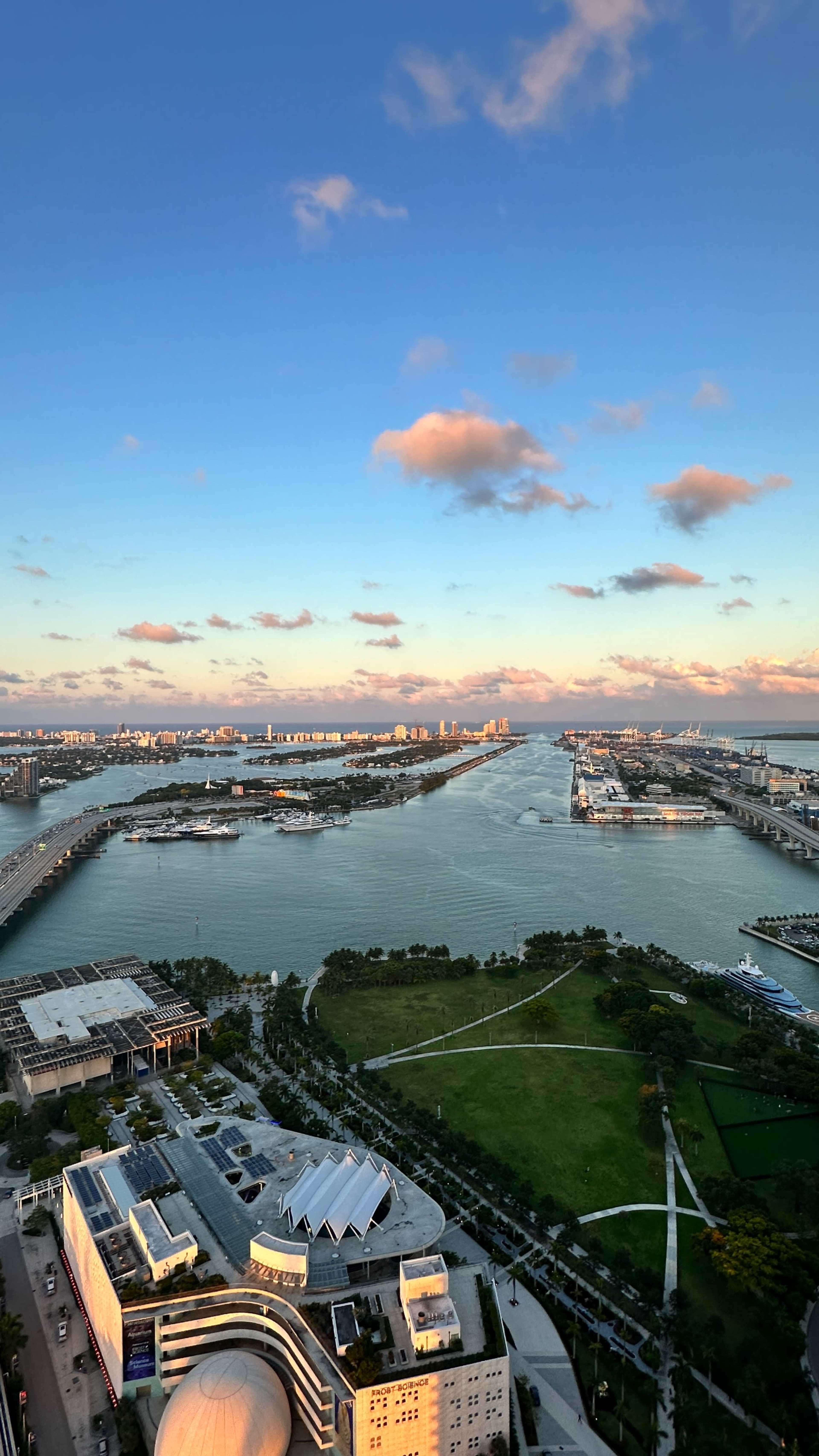 A panoramic view of a waterfront with a mix of bridges and city skyline, surrounded by lush greenery and a blue sky.