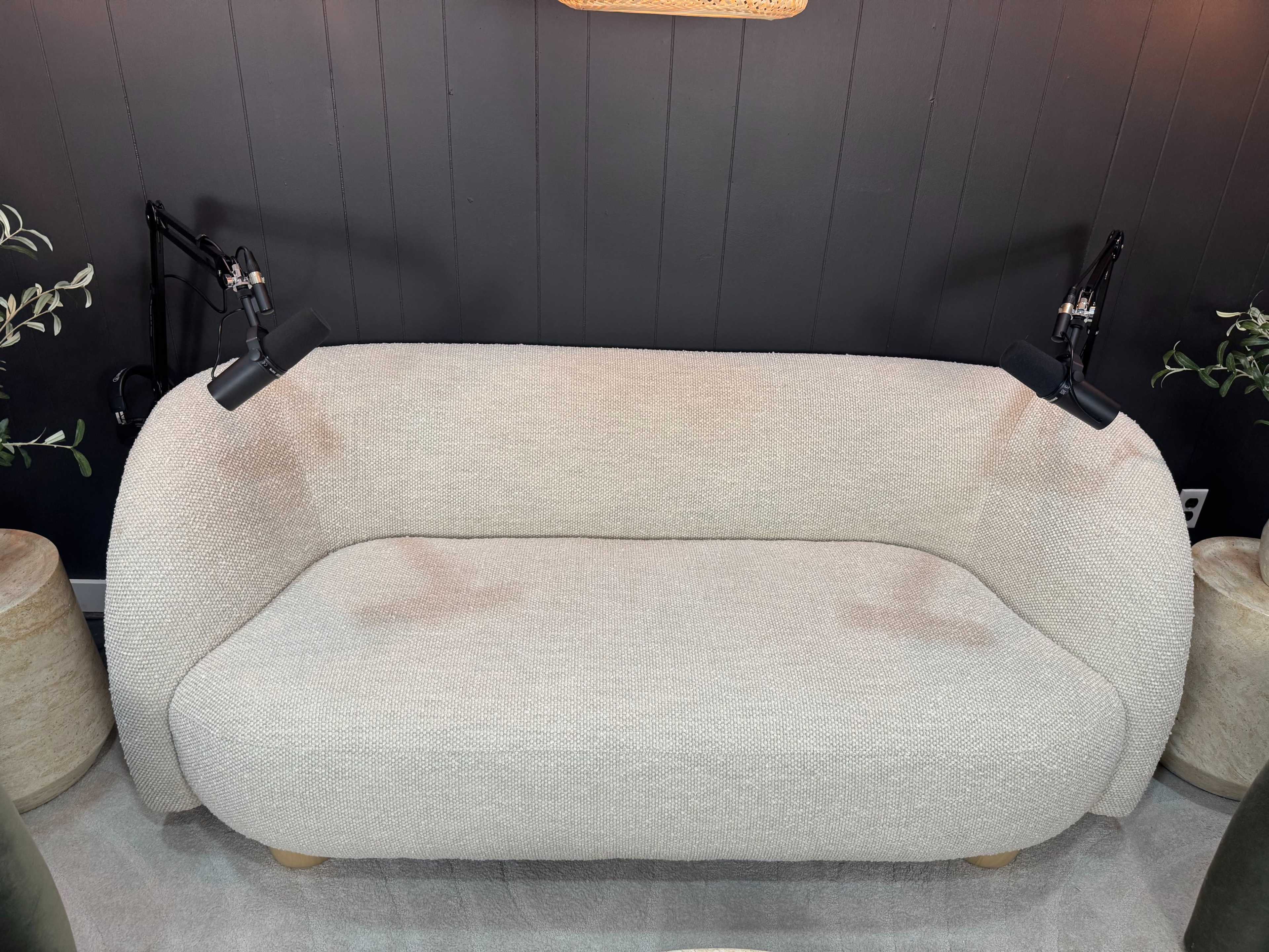 The image shows a light-colored, modern sofa with a curved shape, positioned against a dark wall, and two attached reading lamps on either side.