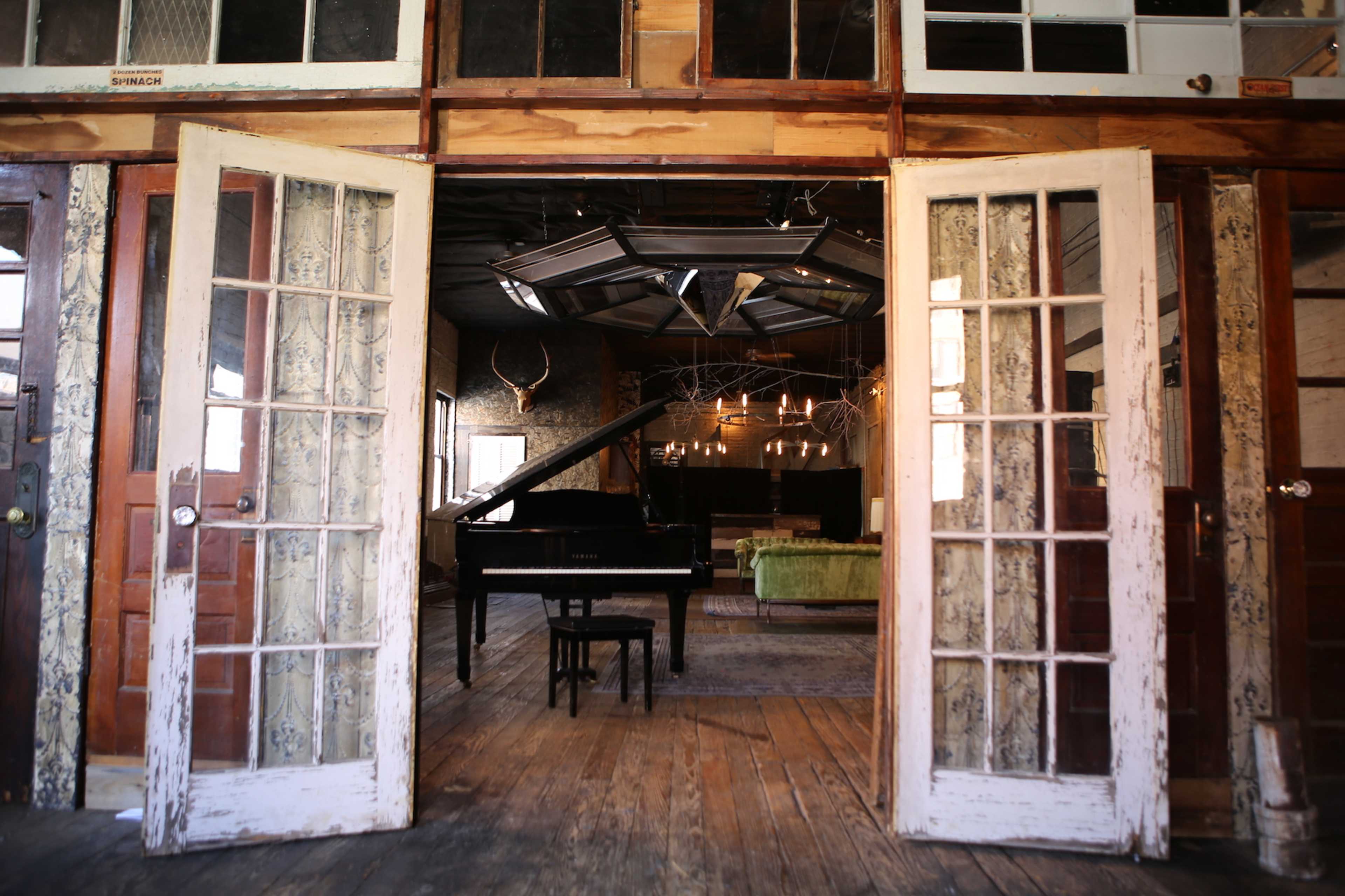 A cozy room with a grand piano and a green sofa, framed by open double doors.