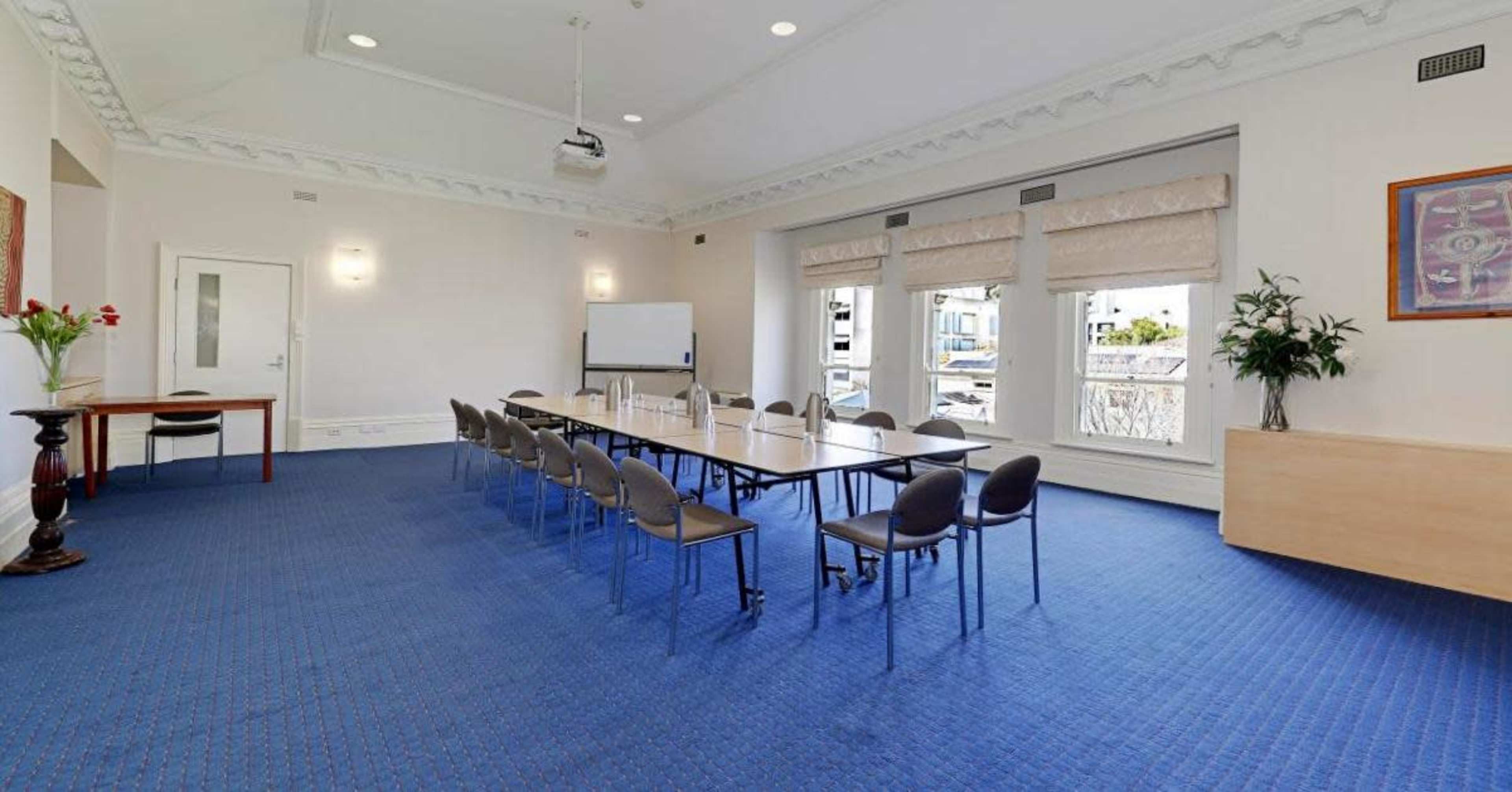 A meeting room features a long table with chairs, large windows, and a projector mounted on the ceiling.