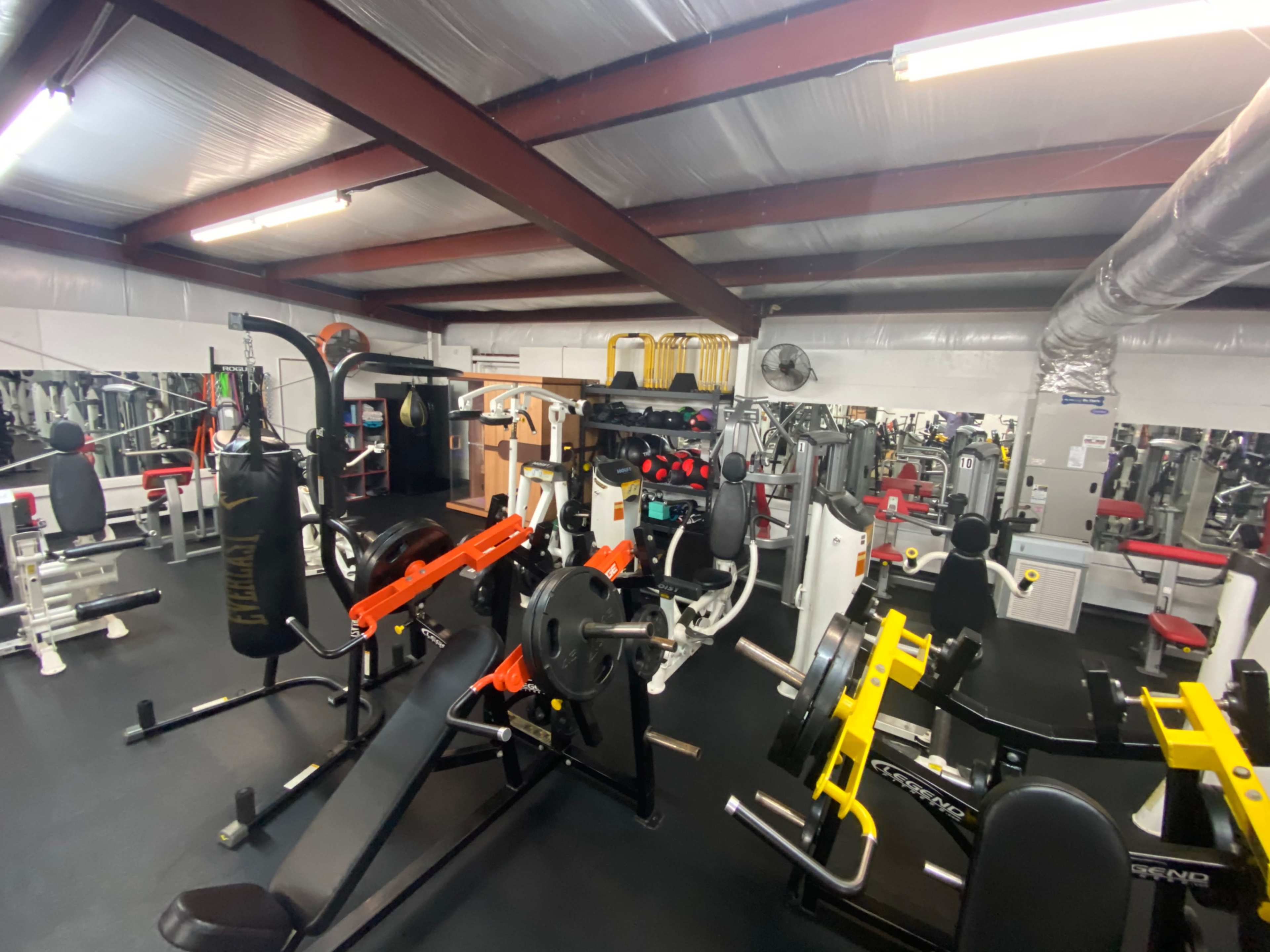 A gym equipped with various weight machines, benches, and cardio equipment arranged under a metal ceiling.
