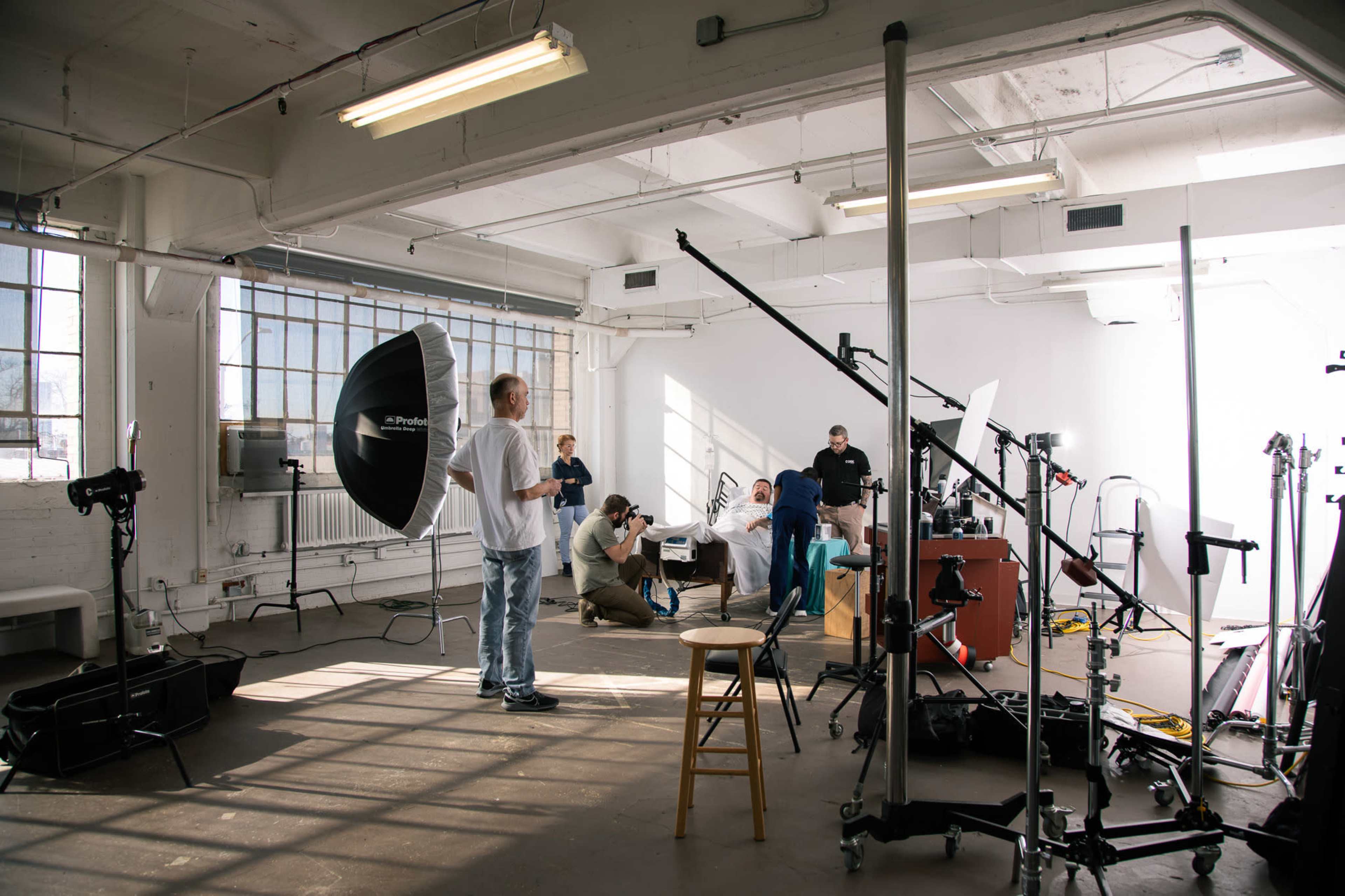 A photography studio is set up with various equipment, including lighting and cameras, while several people are engaged in a photoshoot.