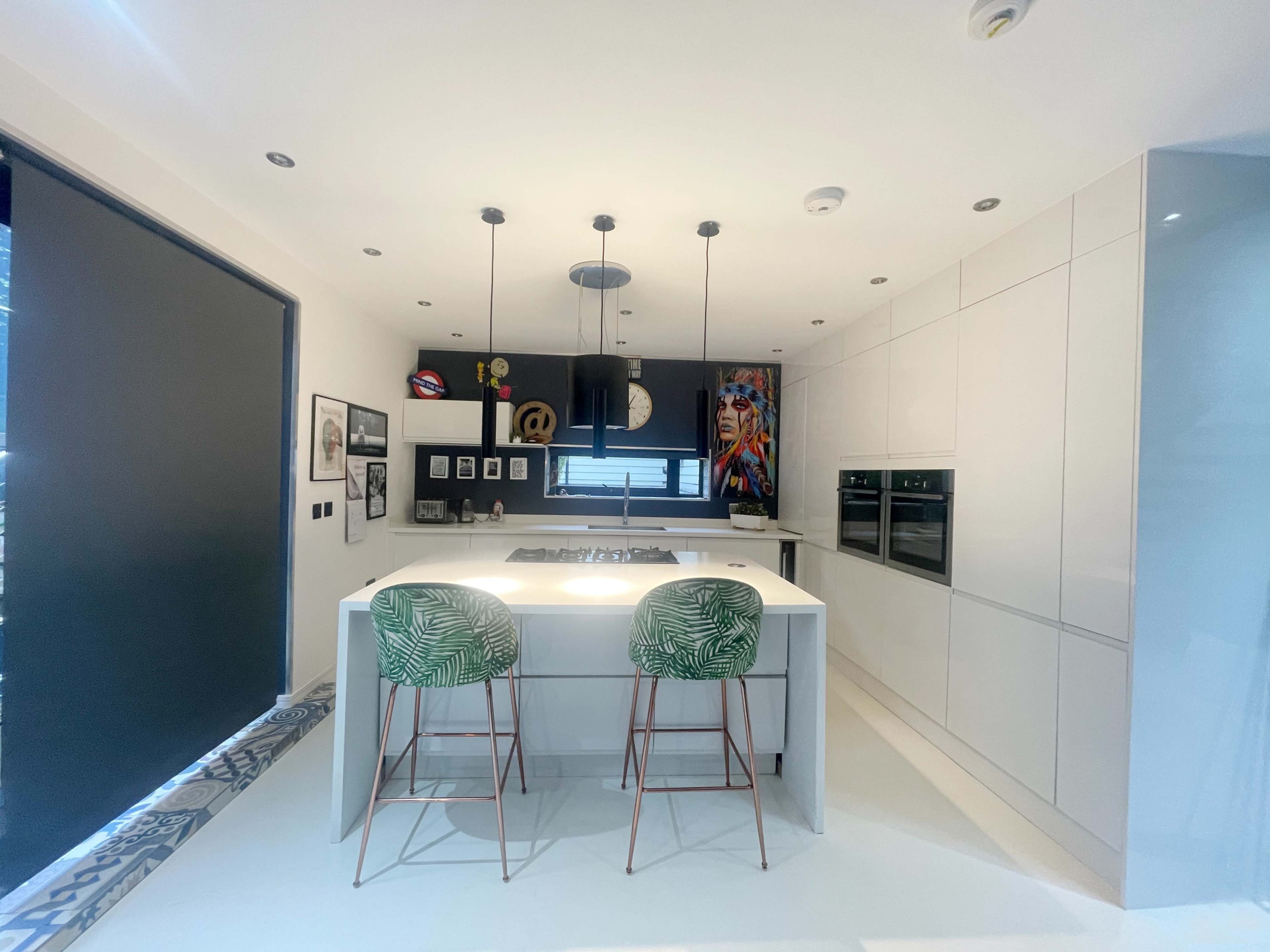 A modern kitchen featuring a central island with bar stools, sleek cabinetry, and wall art.