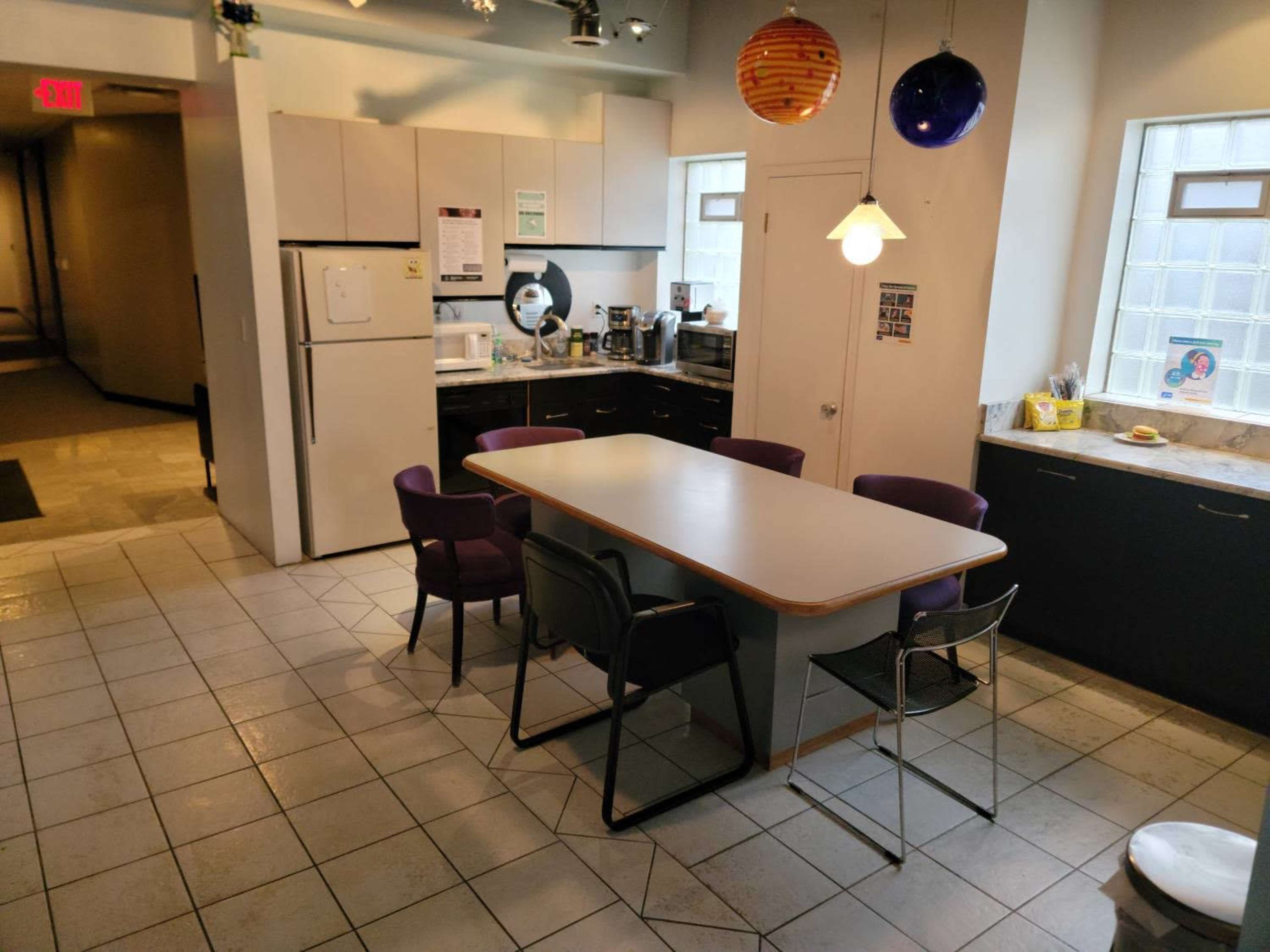 A spacious kitchen features a large dining table surrounded by chairs, with a refrigerator and various appliances visible along the walls.