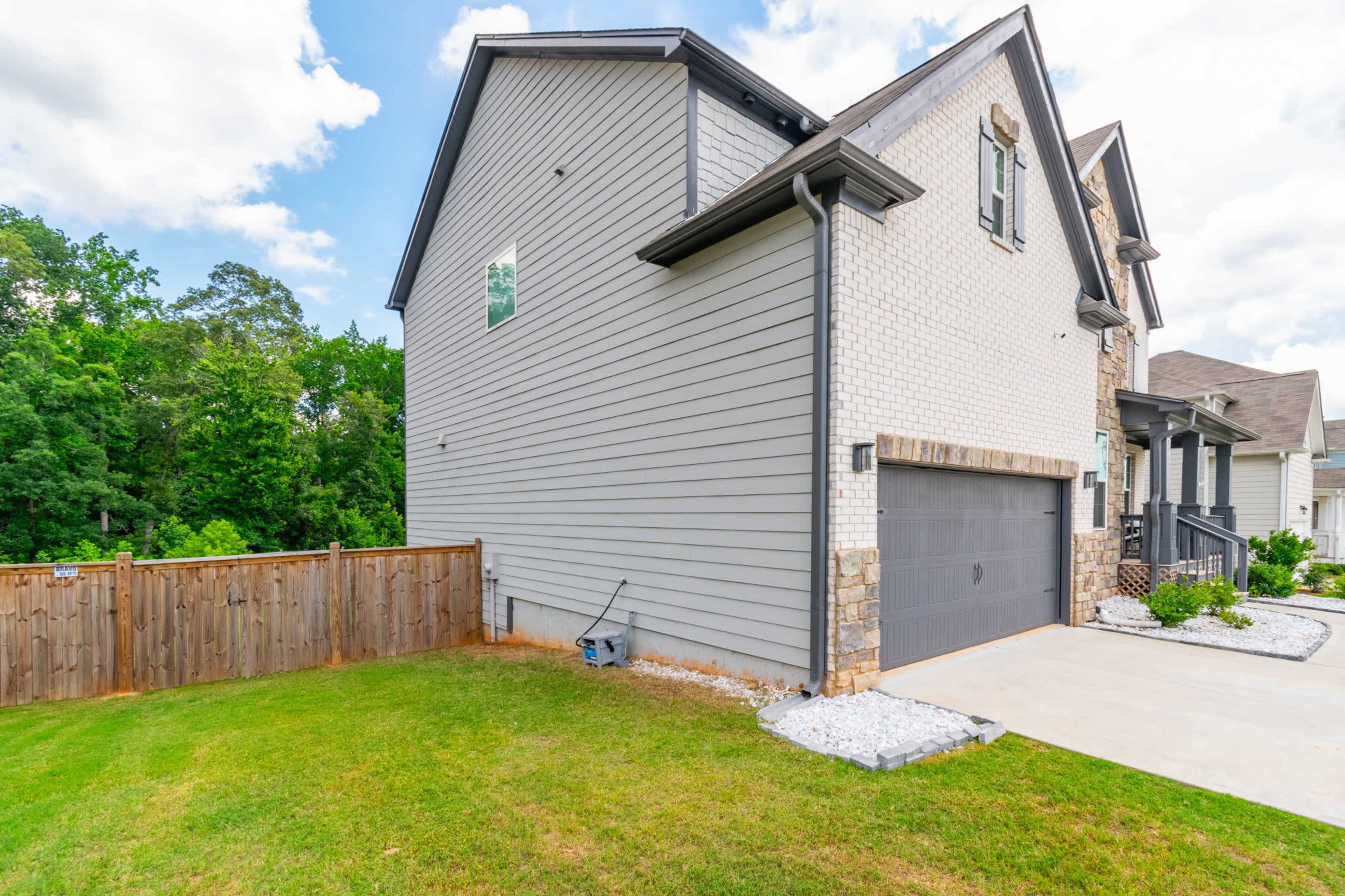 The side of a residential house with a garage, surrounded by a manicured lawn and a wooden fence.