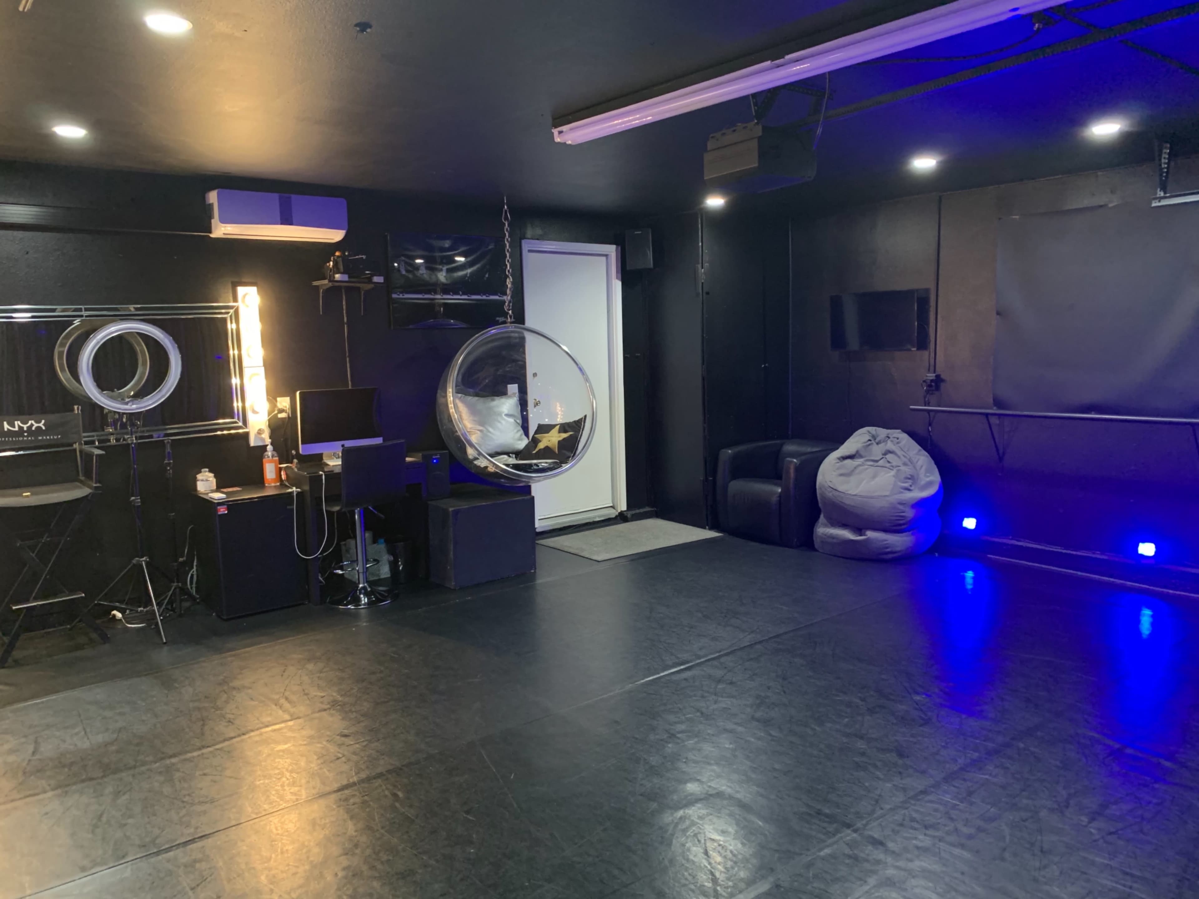 A dark studio space with a large open area, a hanging circular chair, mirrors, and various electronic equipment.