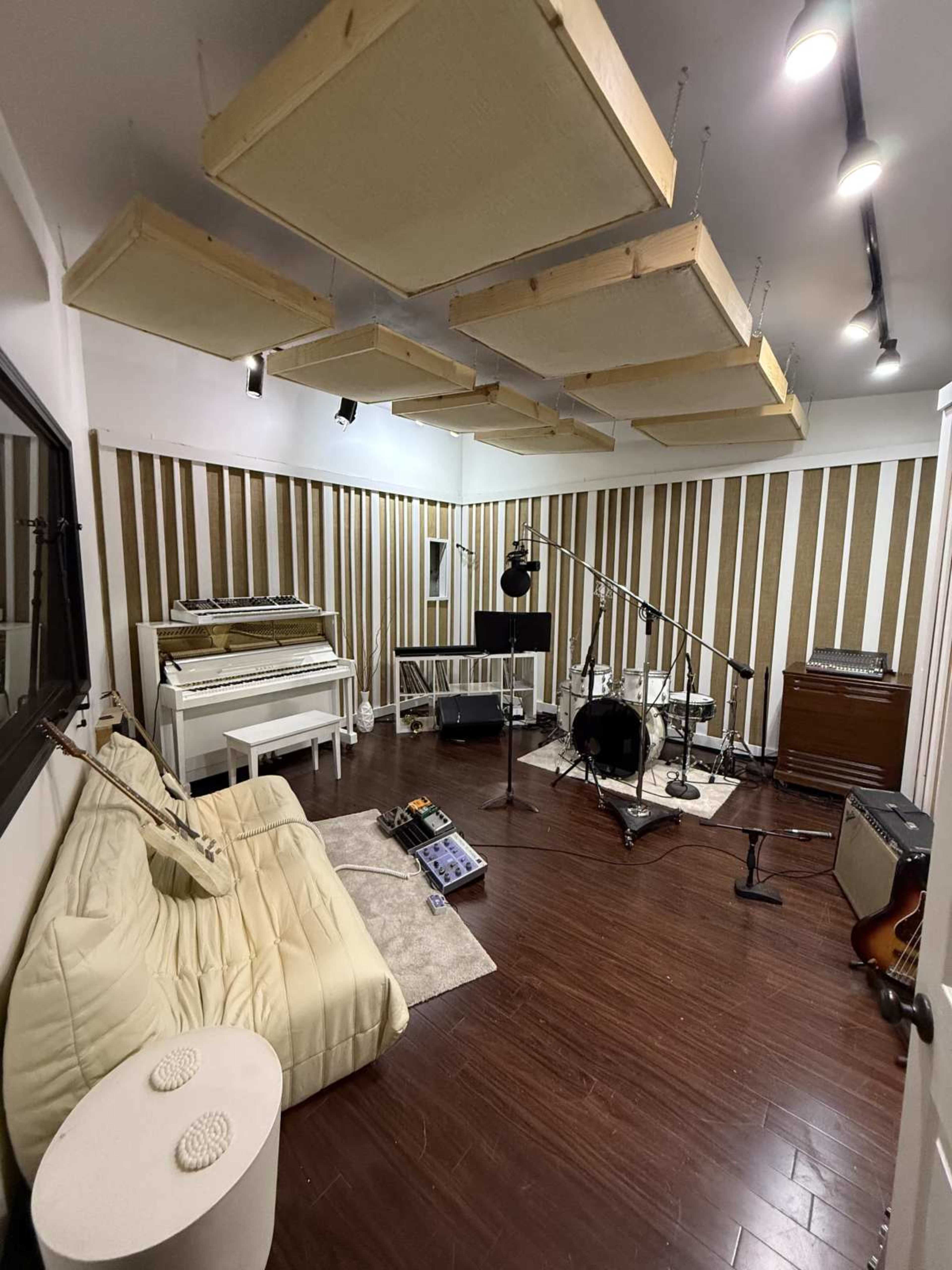 The image shows a sound studio with a white piano, musical instruments, recording equipment, and wooden acoustic panels on the walls.