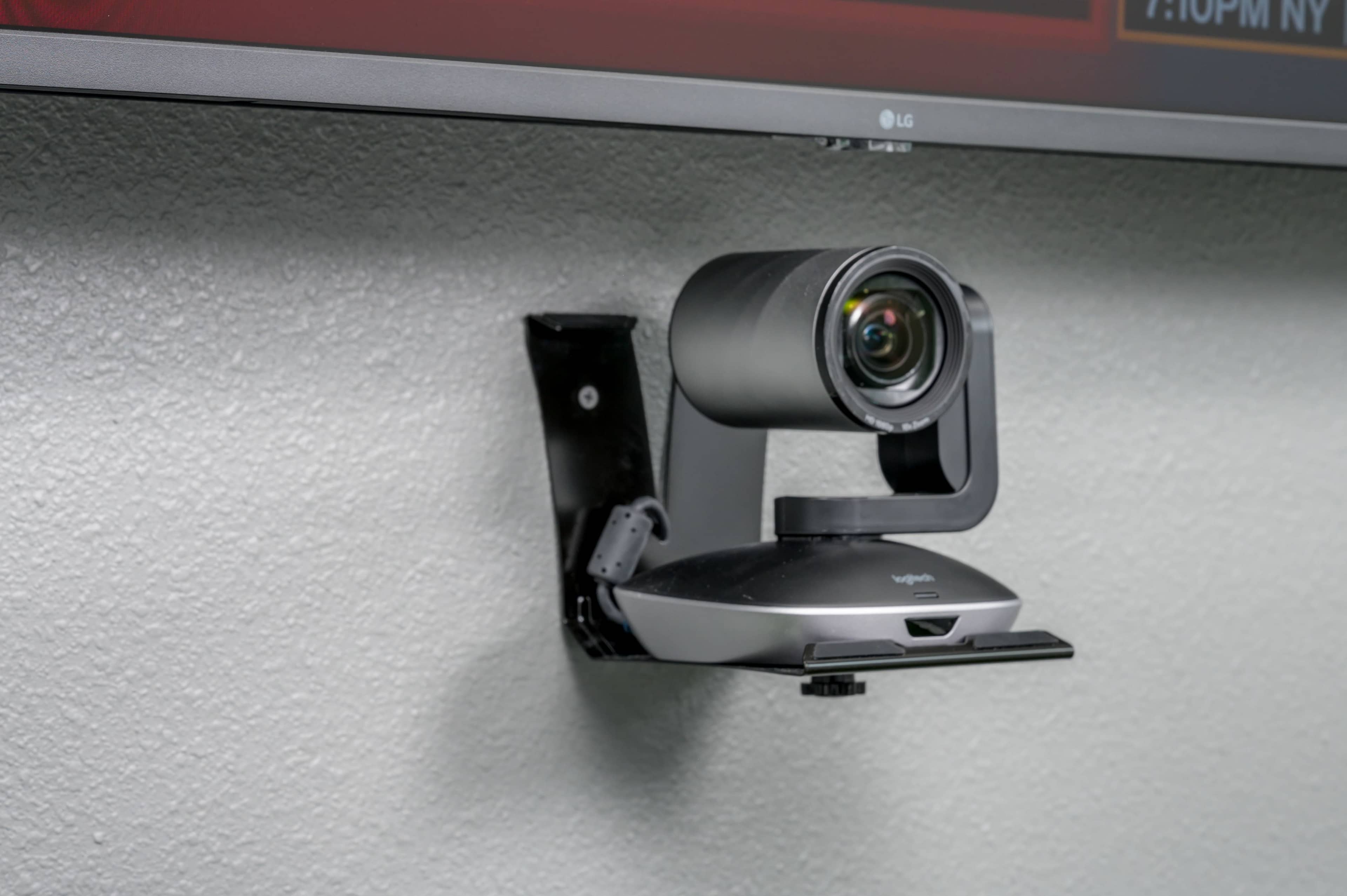 A Logitech camera mounted on a wall beneath a flat-screen TV.