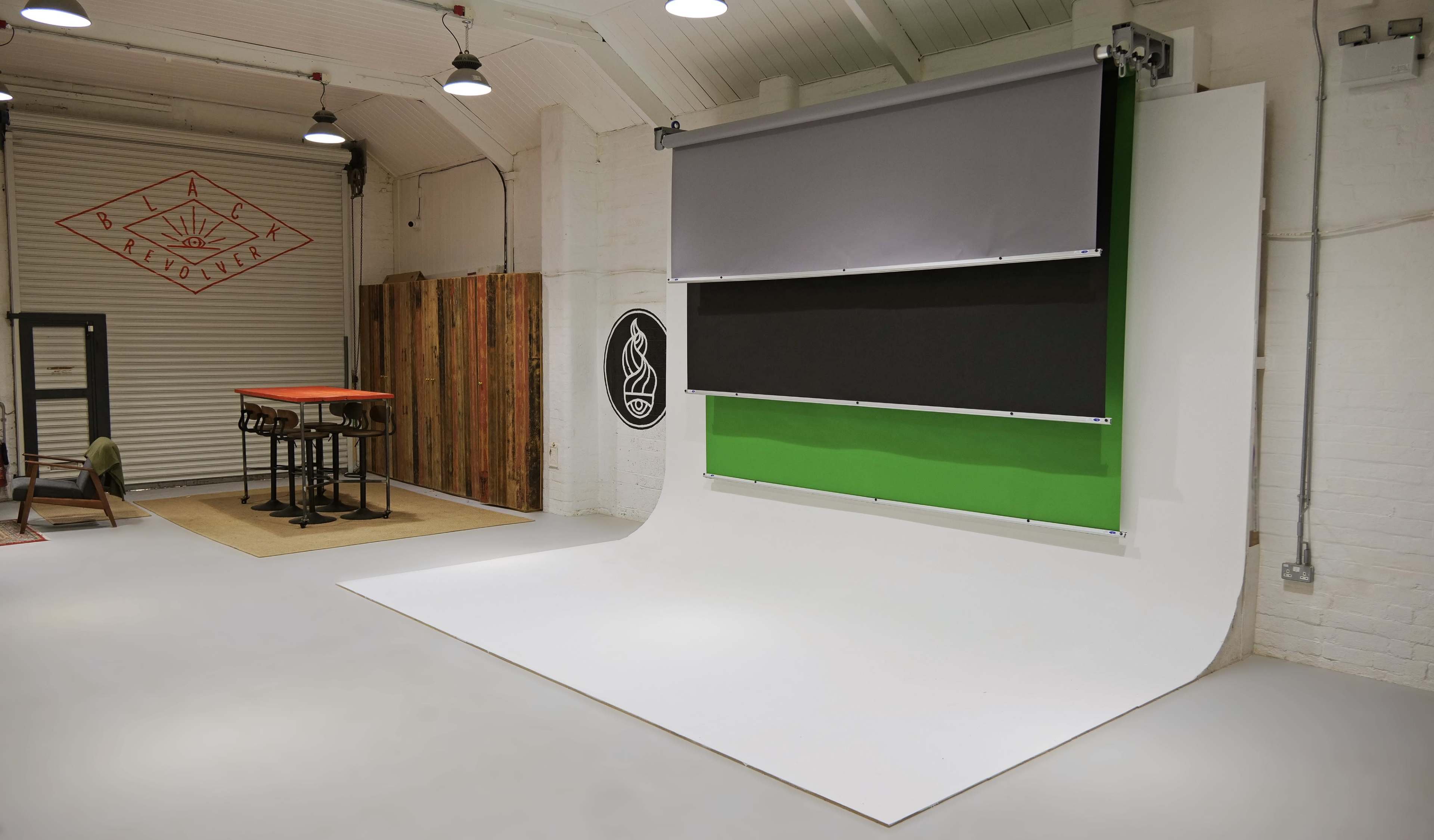 A photography studio with a large, curved backdrop featuring three roll-down color panels: gray, black, and green, along with wooden and metal furnishings in the space.